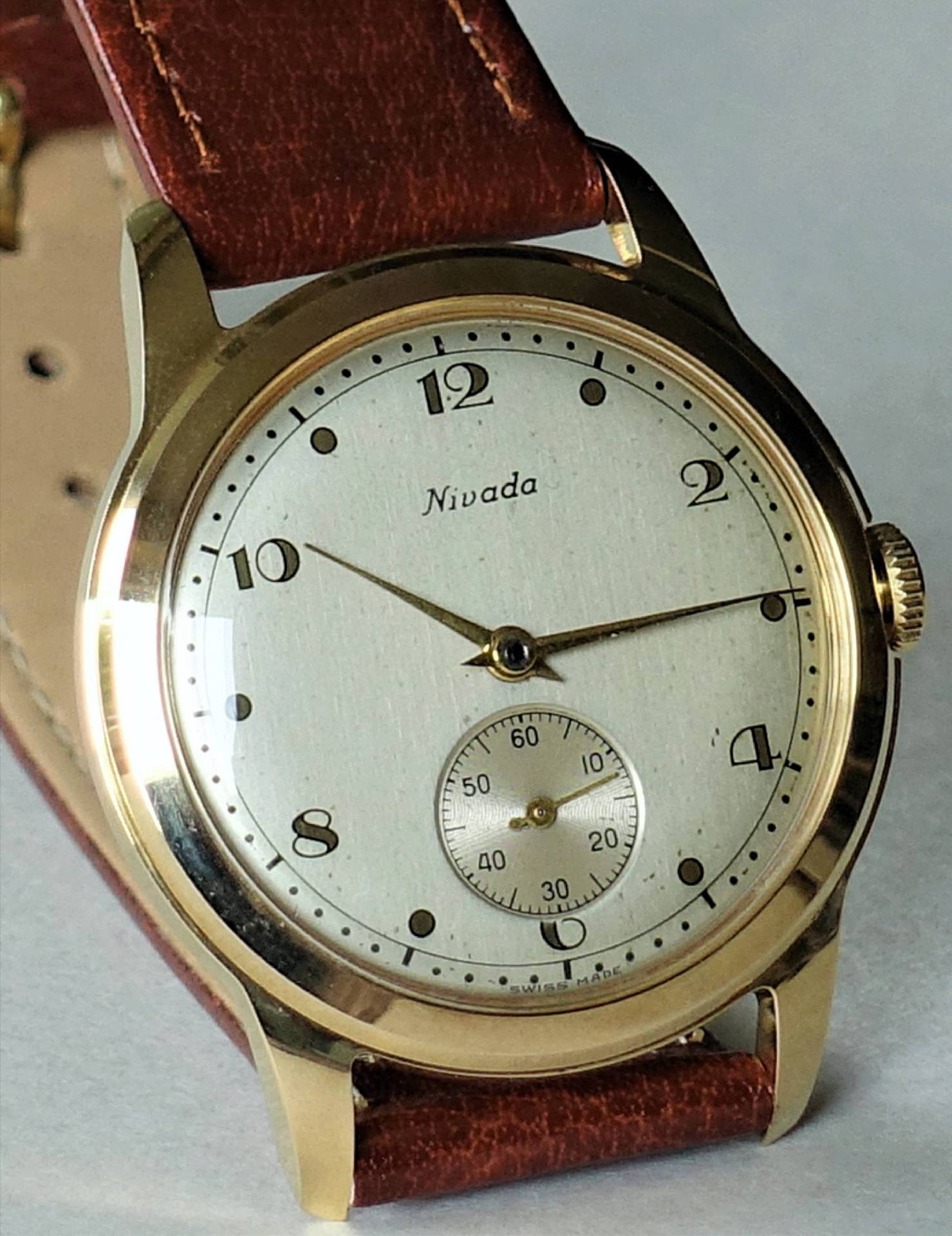 Goldfarbene Armbanduhr mit weißem Zifferblatt und braunem Lederarmband.