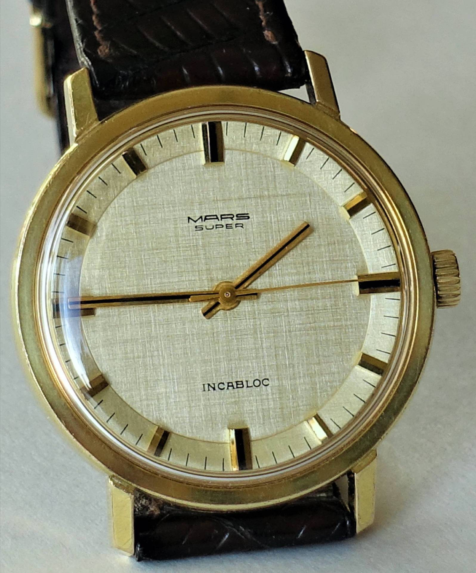 Goldfarbene Armbanduhr mit hellem Zifferblatt und braunem Armband.