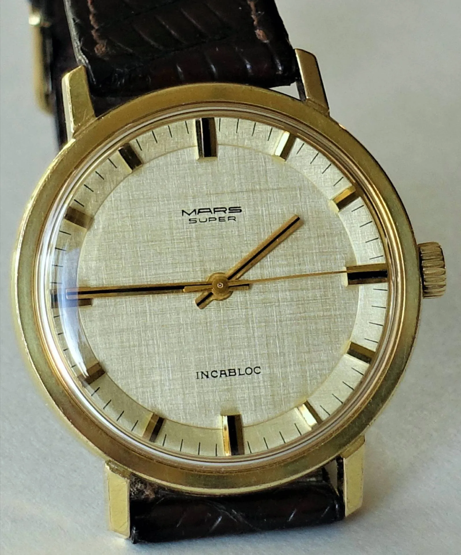 Goldfarbene Armbanduhr mit hellem Zifferblatt und braunem Armband.