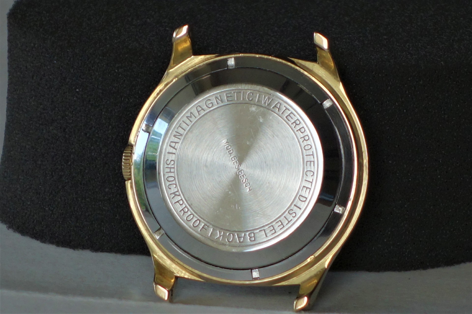 Gehäuse einer Armbanduhr mit goldfarbener Außenseite und silberfarbener Rückseite.