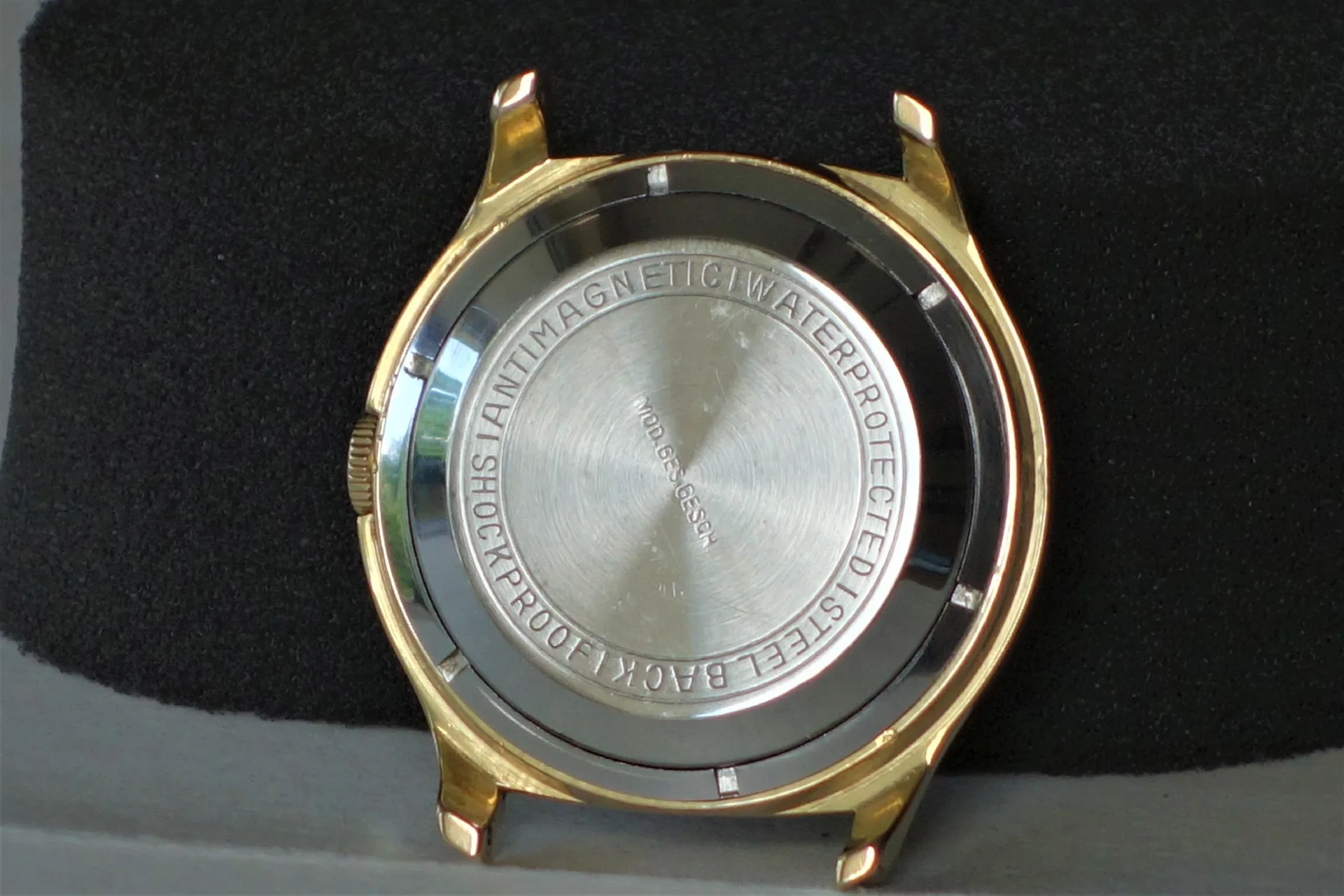 Gehäuse einer Armbanduhr mit goldfarbener Außenseite und silberfarbener Rückseite.