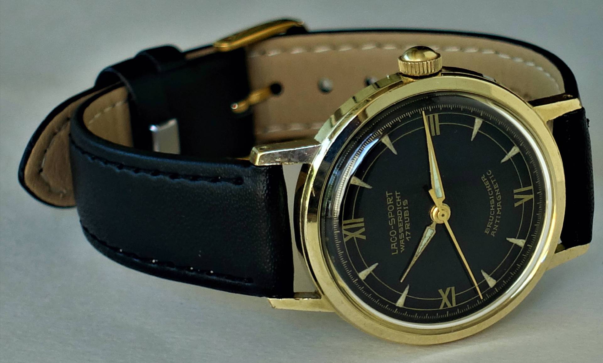 Schwarze Armbanduhr mit goldfarbenem Gehäuse und schwarzem Zifferblatt, Lederarmband.