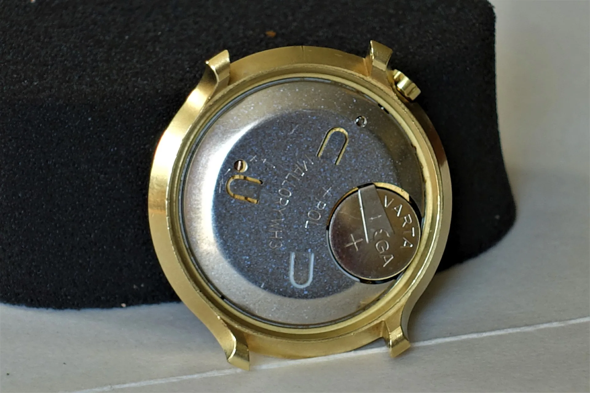 Rundes goldfarbenes Uhrengehäuse mit eingesetztem Quarz-Uhrwerk und sichtbarer Batterie.