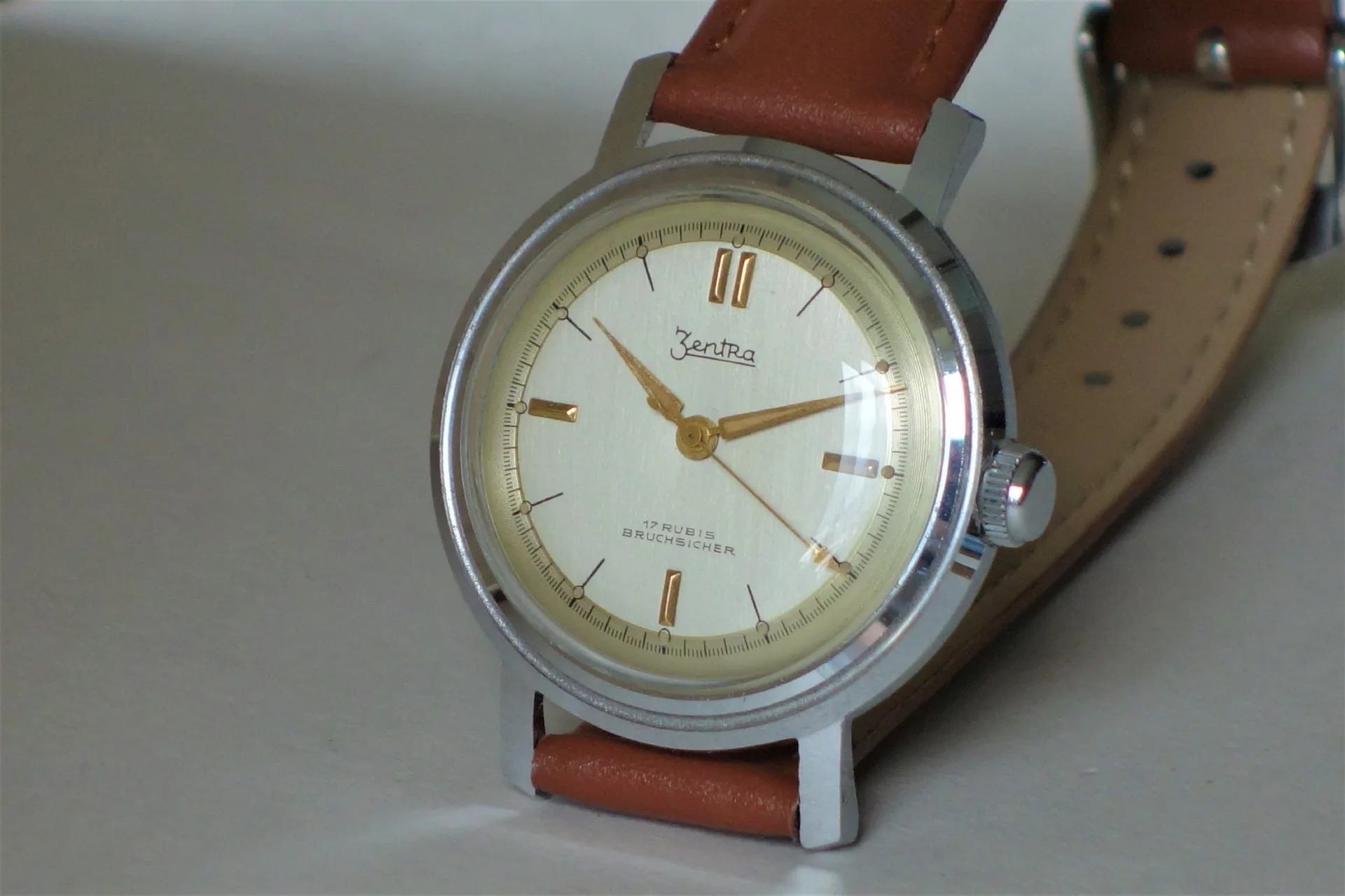 Silberfarbene mechanische Armbanduhr mit beigem Zifferblatt und braunem Armband.