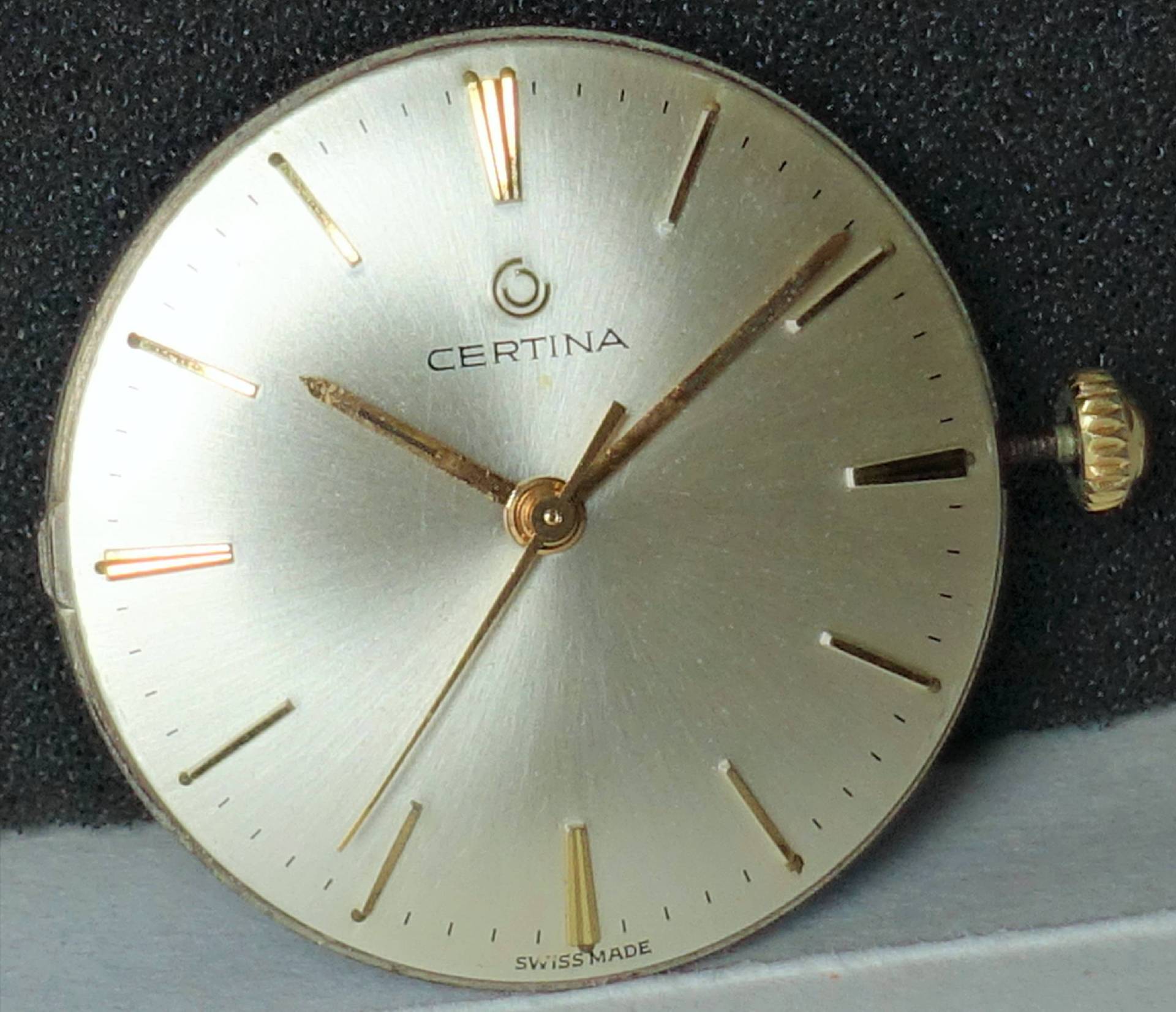 Rundes silberfarbenes Certina Uhrwerk mit goldfarbenen Zeigern und Indizes.