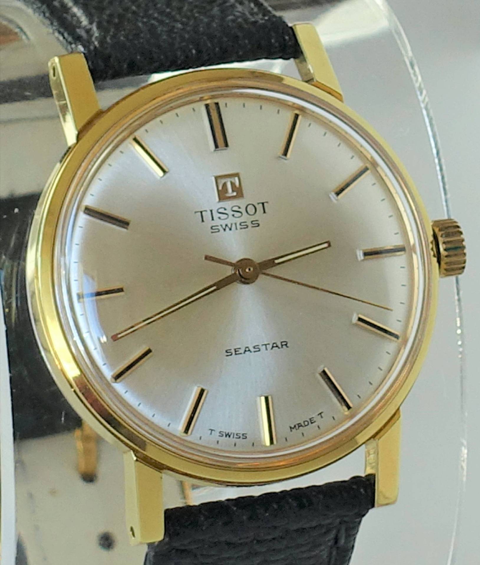 Klassische Armbanduhr mit goldfarbenem Gehäuse, silbernem Zifferblatt und schwarzem Armband.