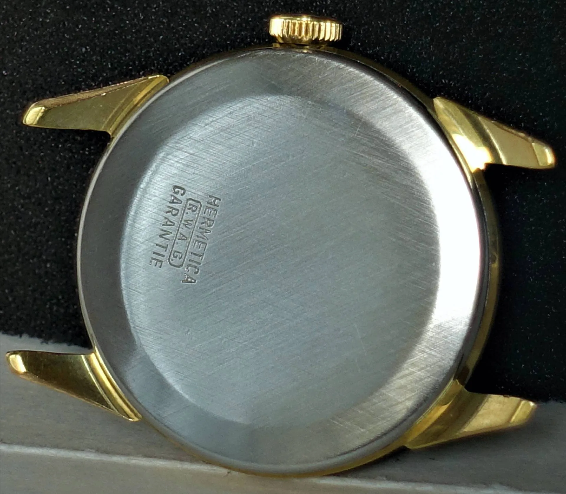 Rundes Uhrengehäuse mit goldfarbener Lünette und silberfarbener Rückseite.