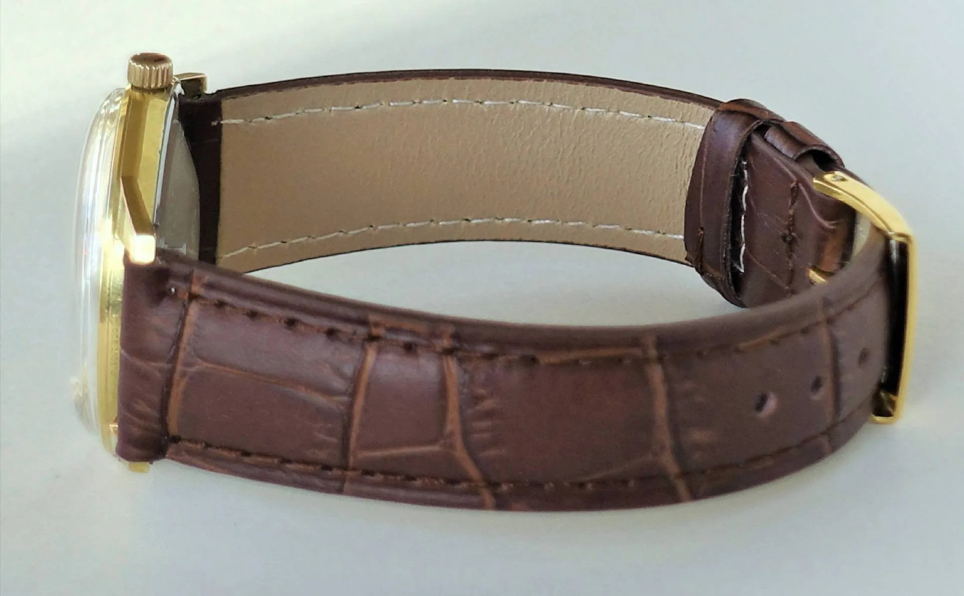 Braunes Lederarmband, gelbes Gehäuse Eine Armbanduhr mit braunem Lederarmband und einem gelbfarbenen Gehäuse liegt auf einer hellen Oberfläche.