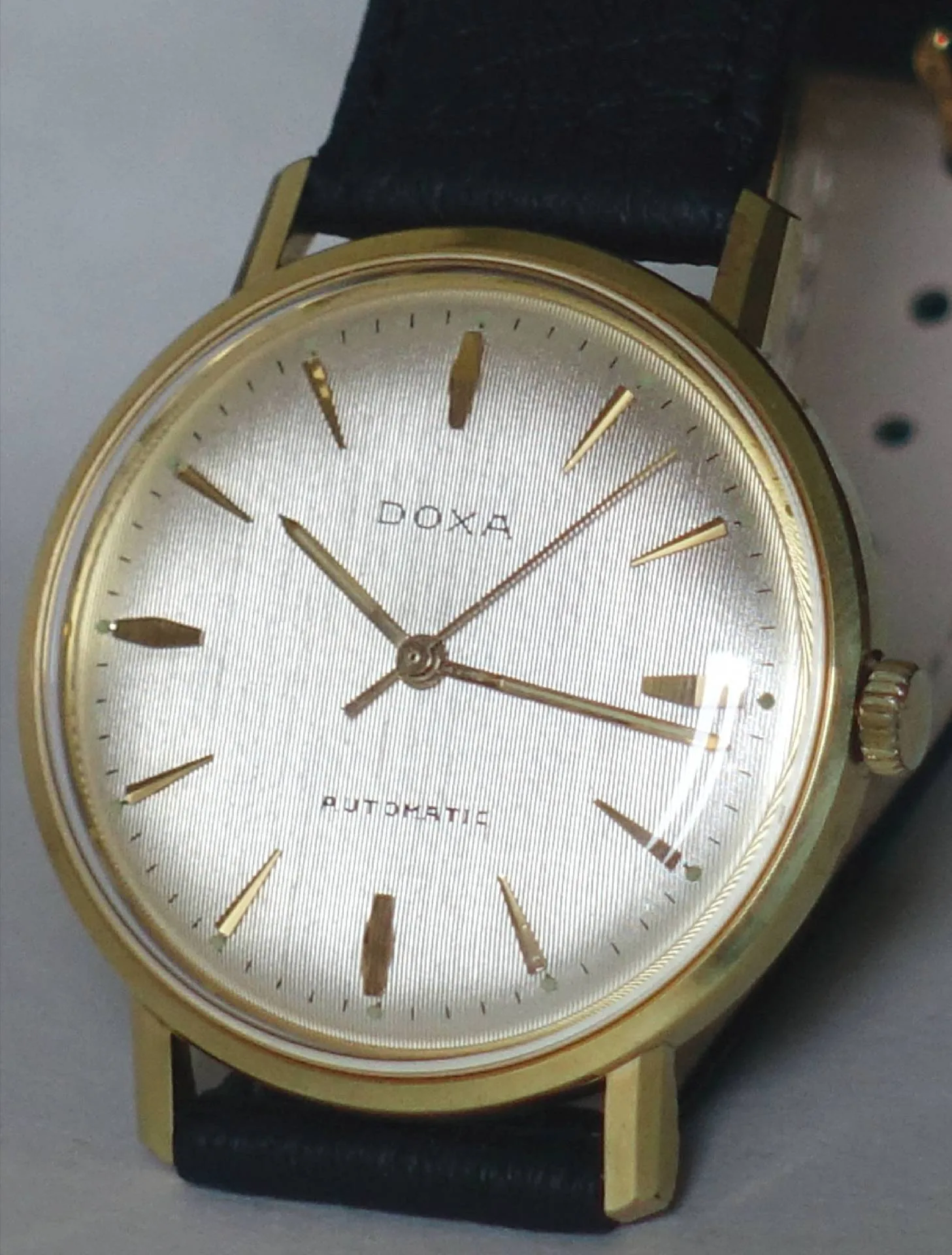 Doxa Armbanduhr goldfarben Goldfarbene Doxa Armbanduhr mit hellem Zifferblatt und schwarzem Armband.