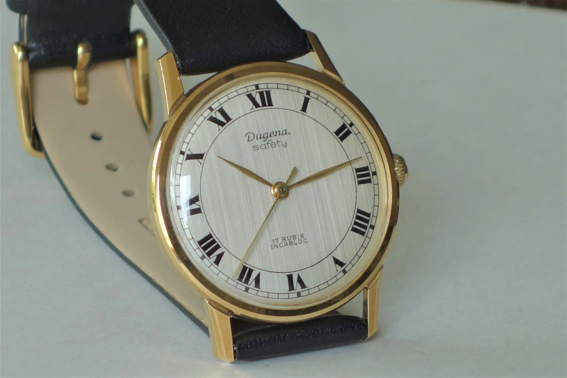 Runde Armbanduhr mit goldfarbenem Gehäuse, hellem Zifferblatt mit römischen Zahlen und schwarzem Armband.