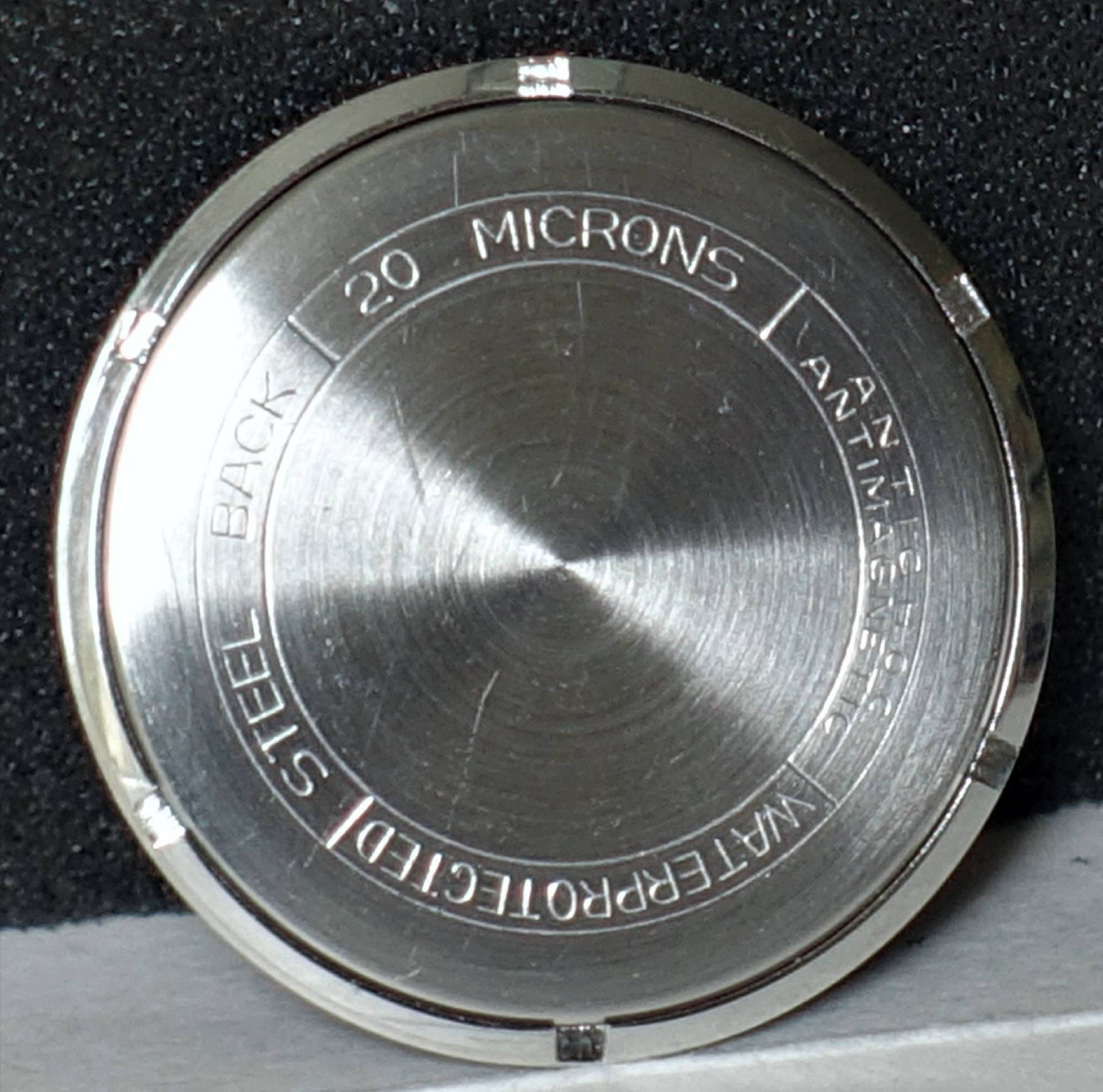 Runder silberfarbener Uhrenboden aus Metall mit Gravur.