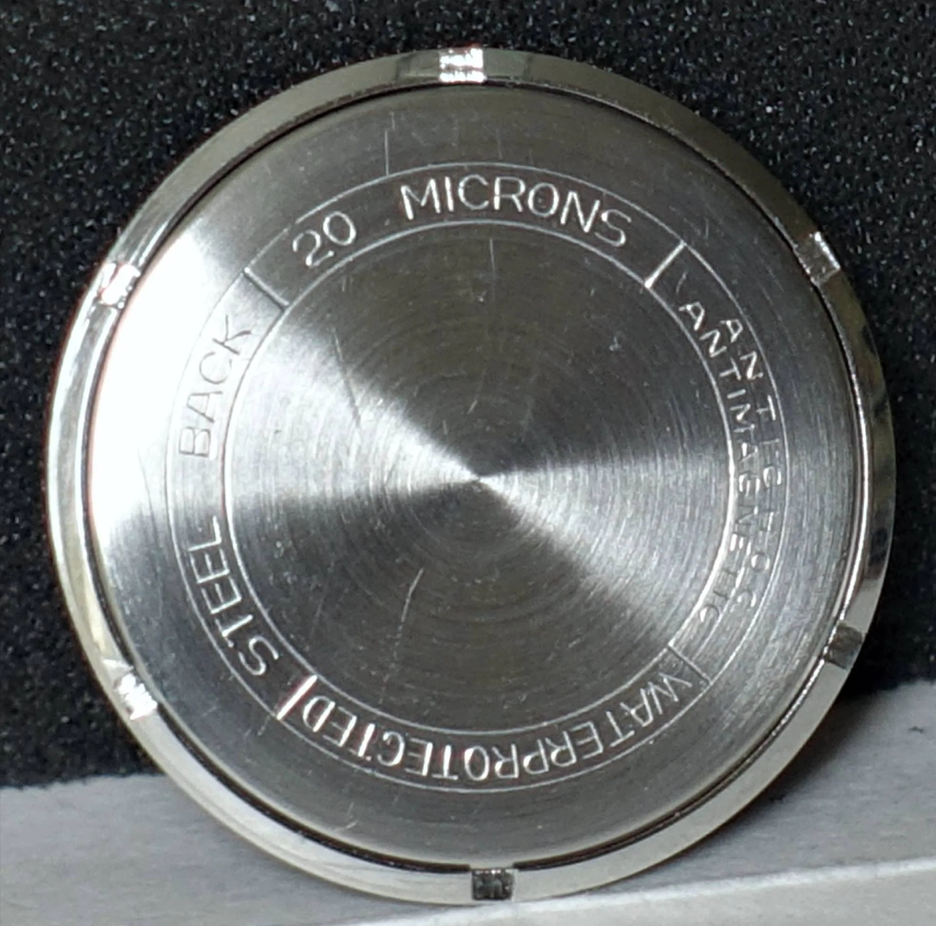 Runder silberfarbener Uhrenboden aus Metall mit Gravur.