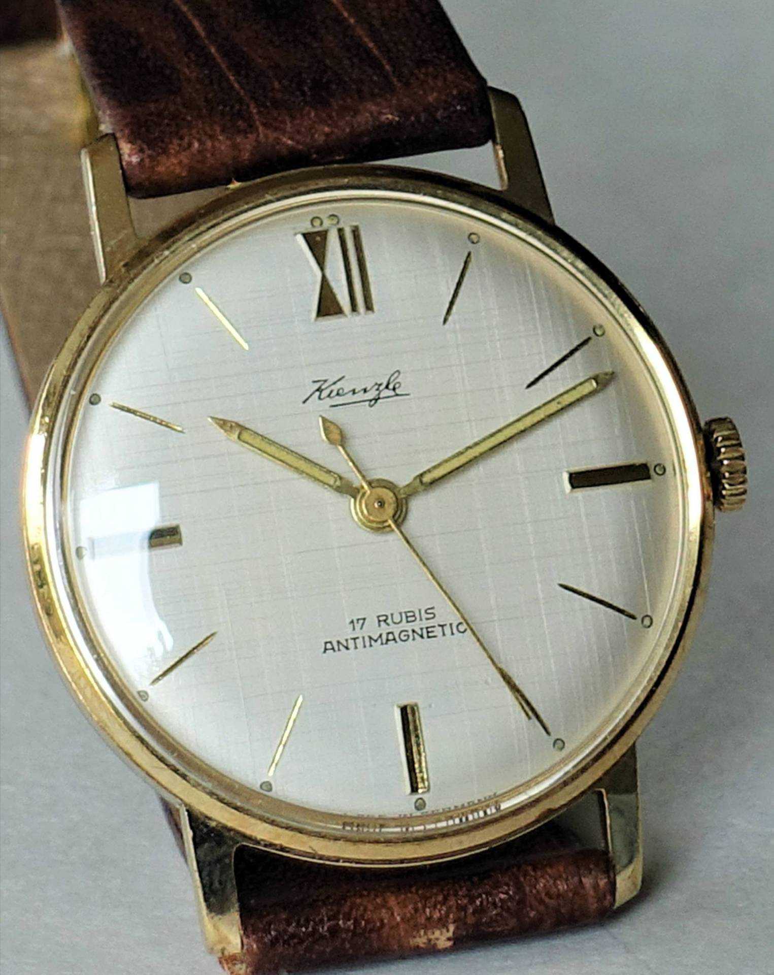 Goldfarbene Armbanduhr mit weißem Zifferblatt und braunem Lederarmband.
