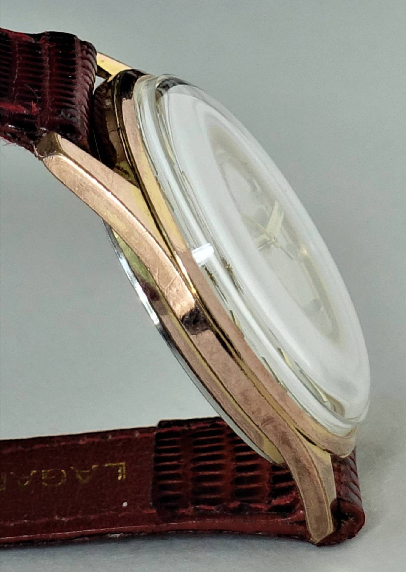 Goldfarbene Armbanduhr mit braunem Armband und gewölbtem Uhrglas.