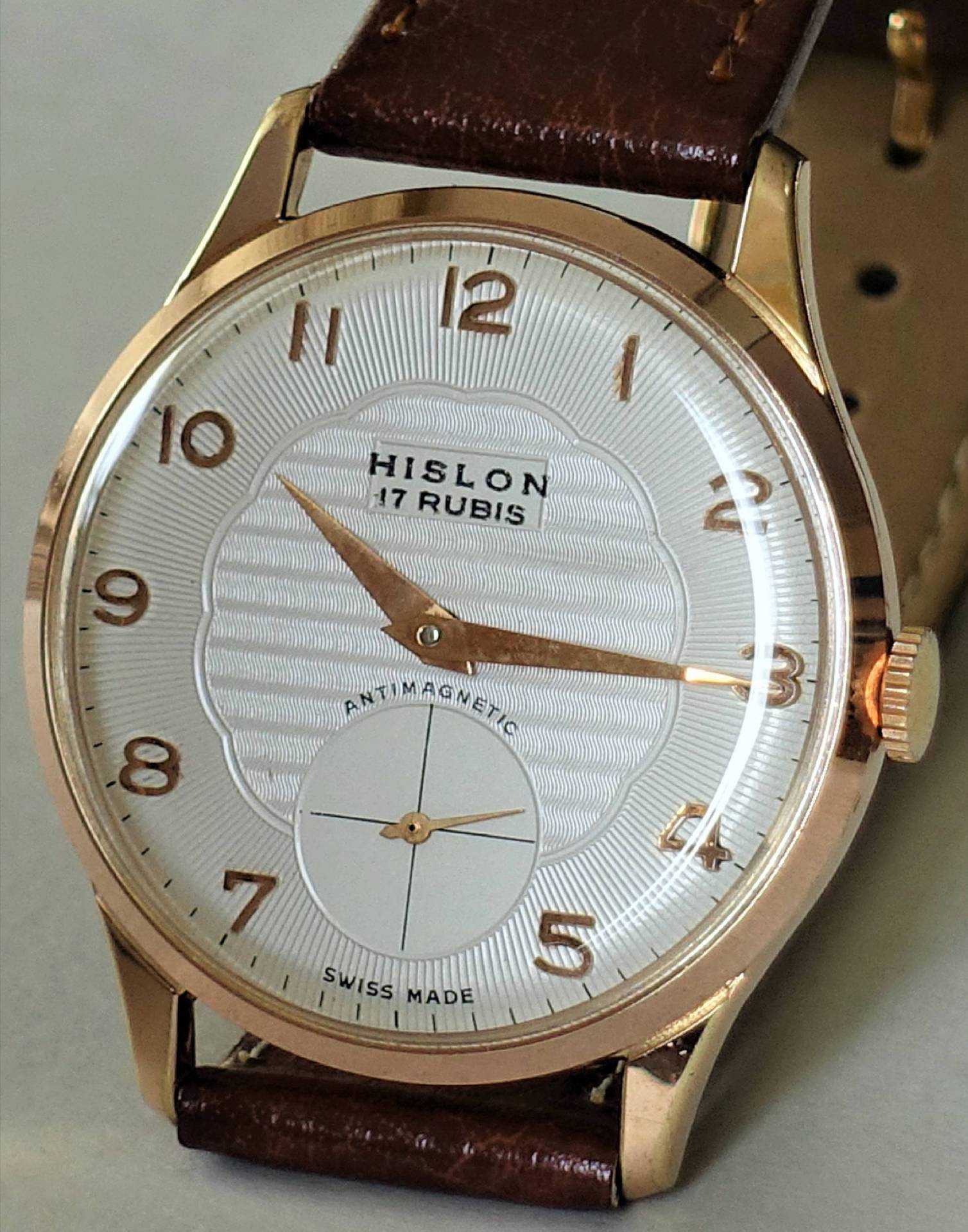 Eine klassische Armbanduhr mit weißem Zifferblatt, goldfarbenem Gehäuse und Zeigern sowie braunem Lederarmband.