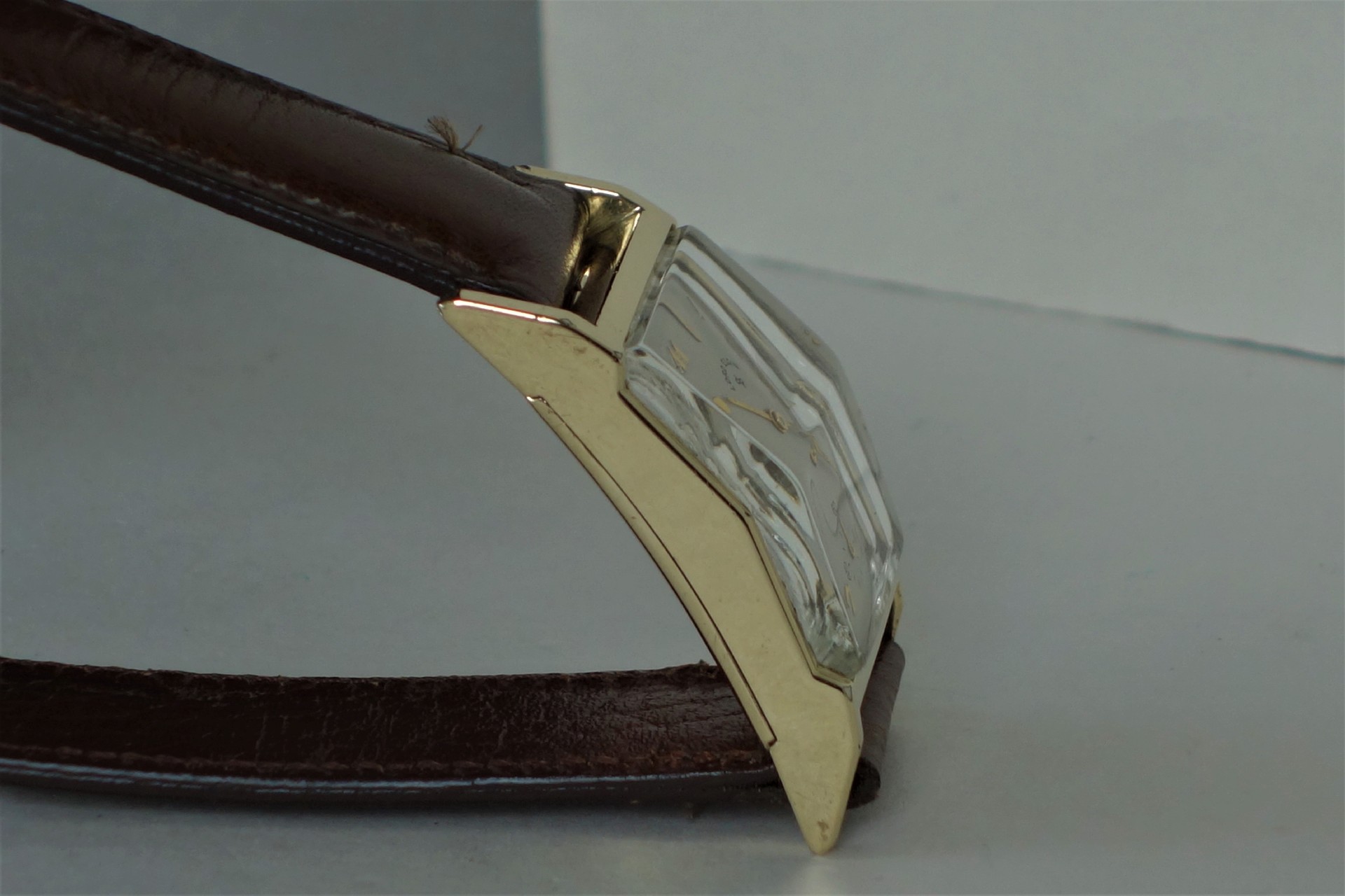 Rechteckige Armbanduhr mit goldfarbenem Gehäuse und braunem Lederarmband.