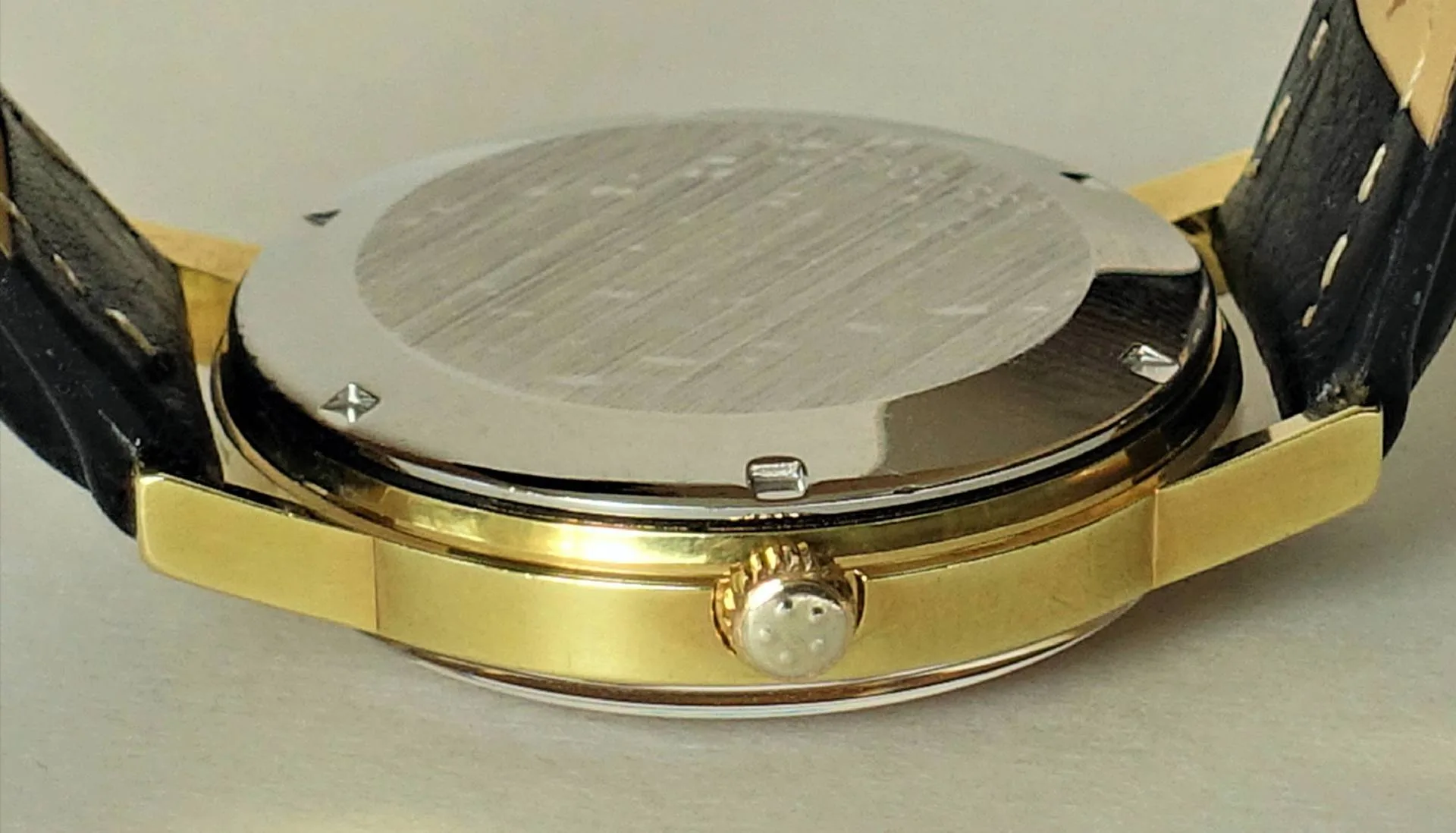 Rückseite eines goldfarbenen Uhrgehäuses mit silberfarbener Abdeckung und schwarzem Armband.
