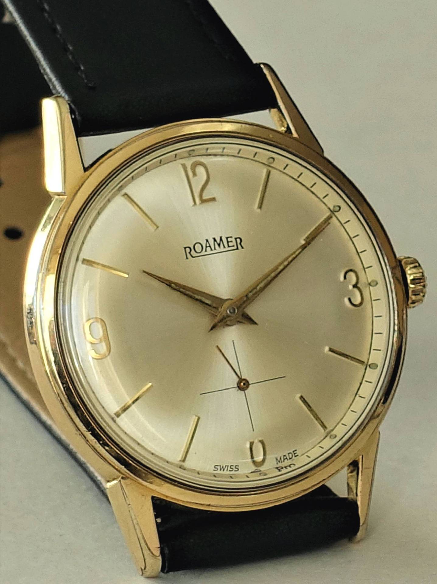 Goldfarbene Armbanduhr mit hellem Zifferblatt und schwarzem Lederarmband.