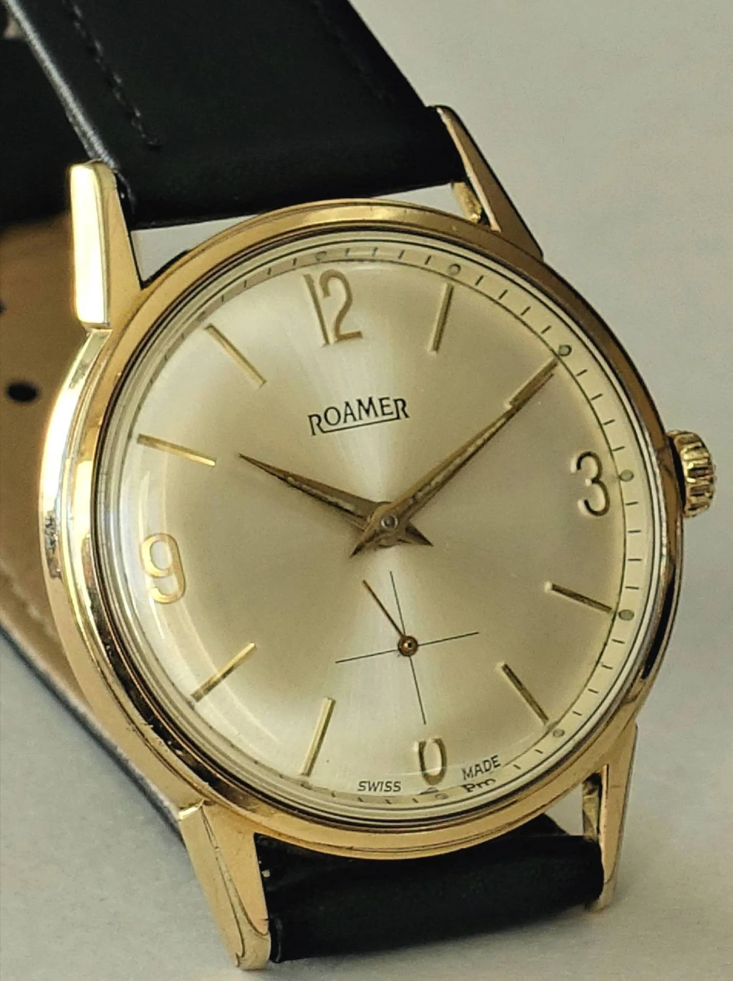 Goldfarbene Armbanduhr mit hellem Zifferblatt und schwarzem Lederarmband.