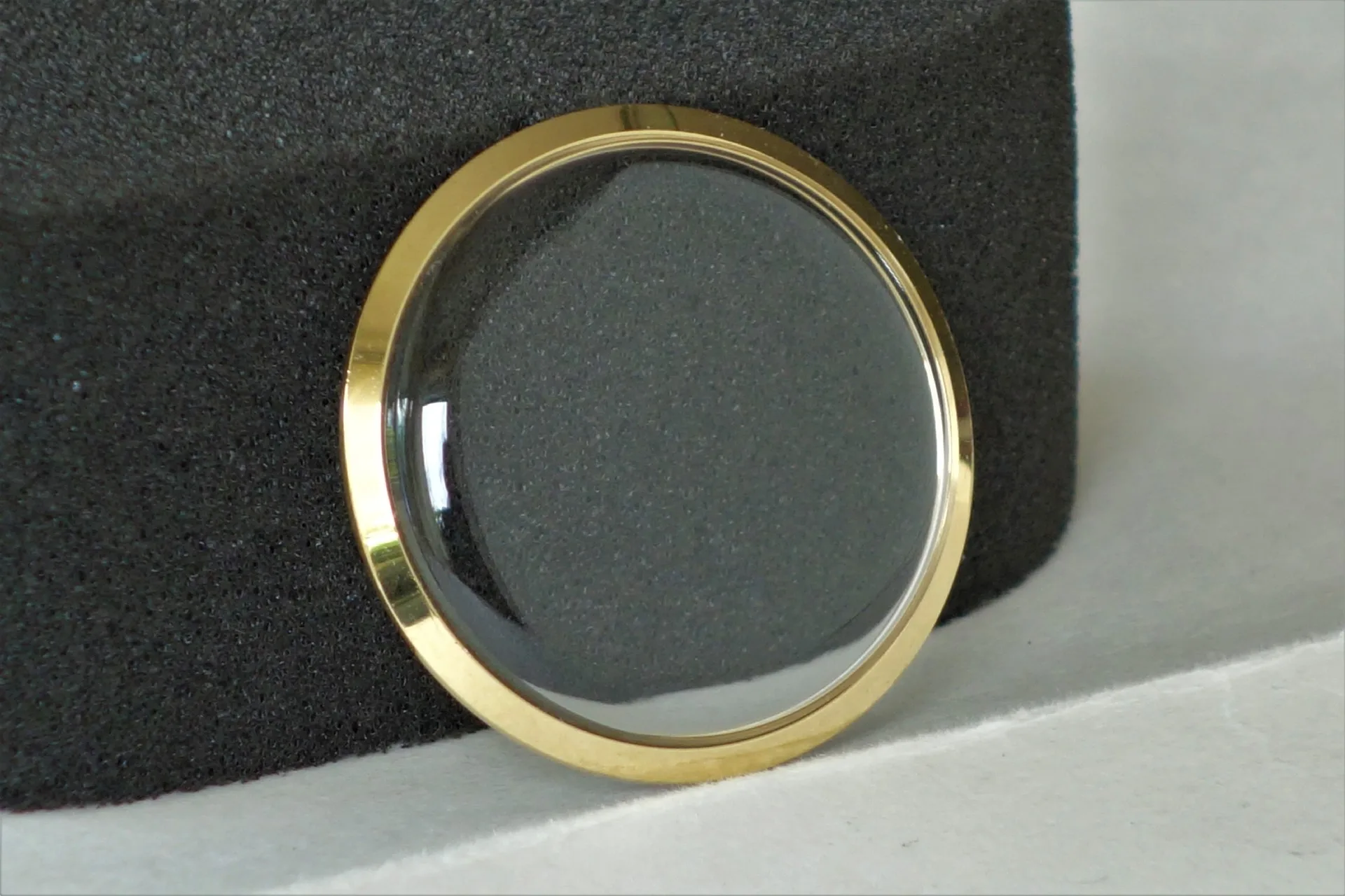 Rundes, transparentes Uhrglas mit einem goldfarbenen Rand.