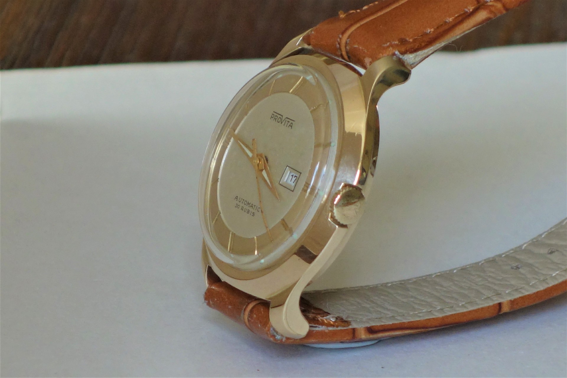 Beige Armbanduhr mit rundem Zifferblatt und braunem Lederarmband.