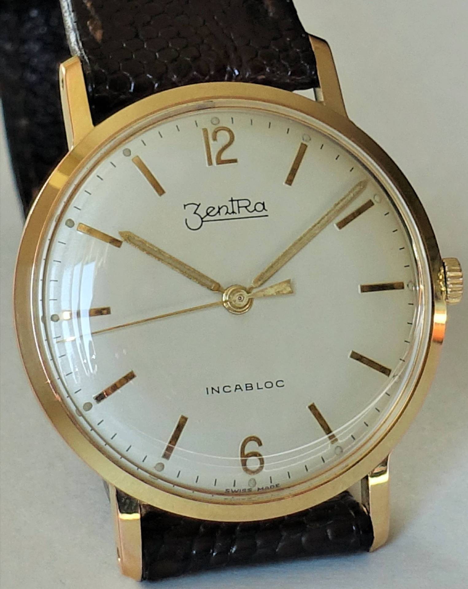 Goldfarbene Armbanduhr mit weißem Zifferblatt und braunem Armband.