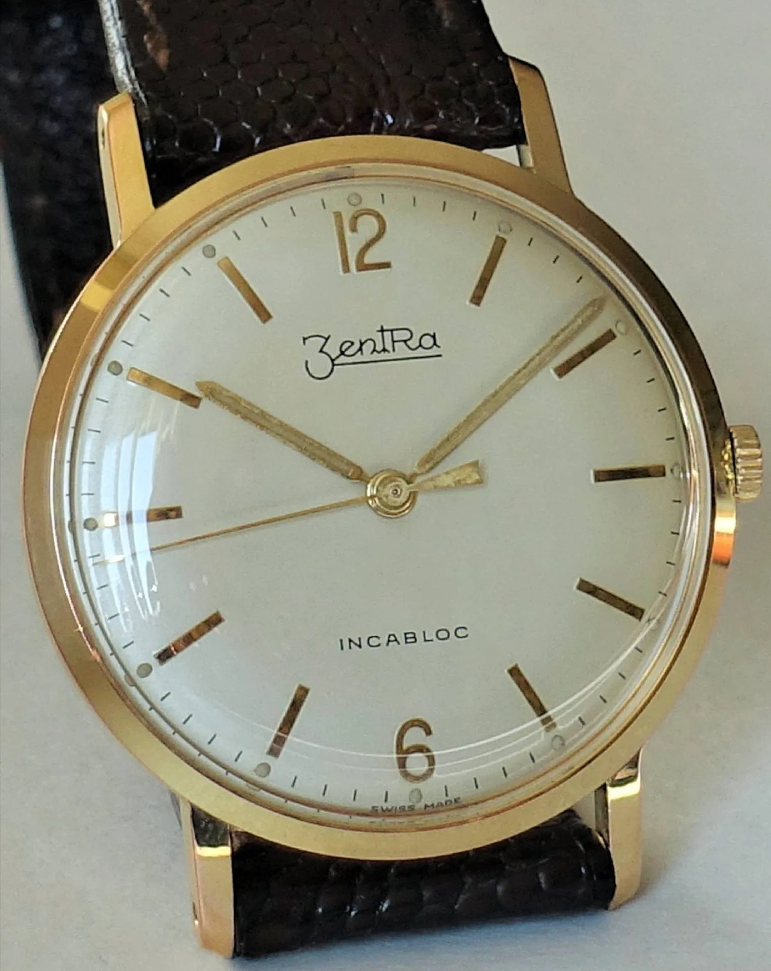Goldfarbene Armbanduhr mit weißem Zifferblatt und braunem Armband.
