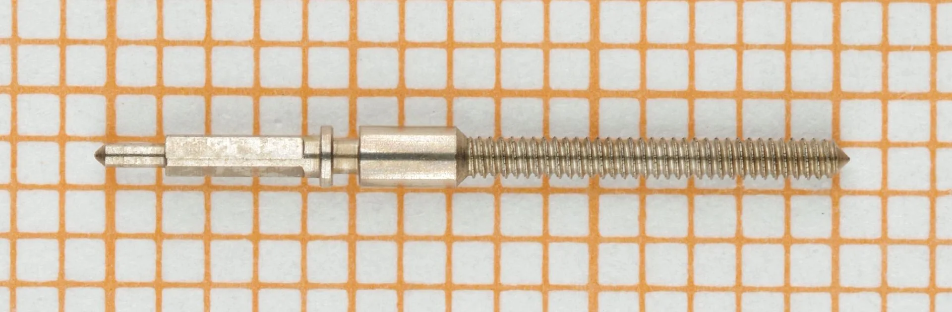 Silberfarbene Aufzugswelle aus Edelstahl für Armbanduhren, auf Millimeterpapier fotografiert.