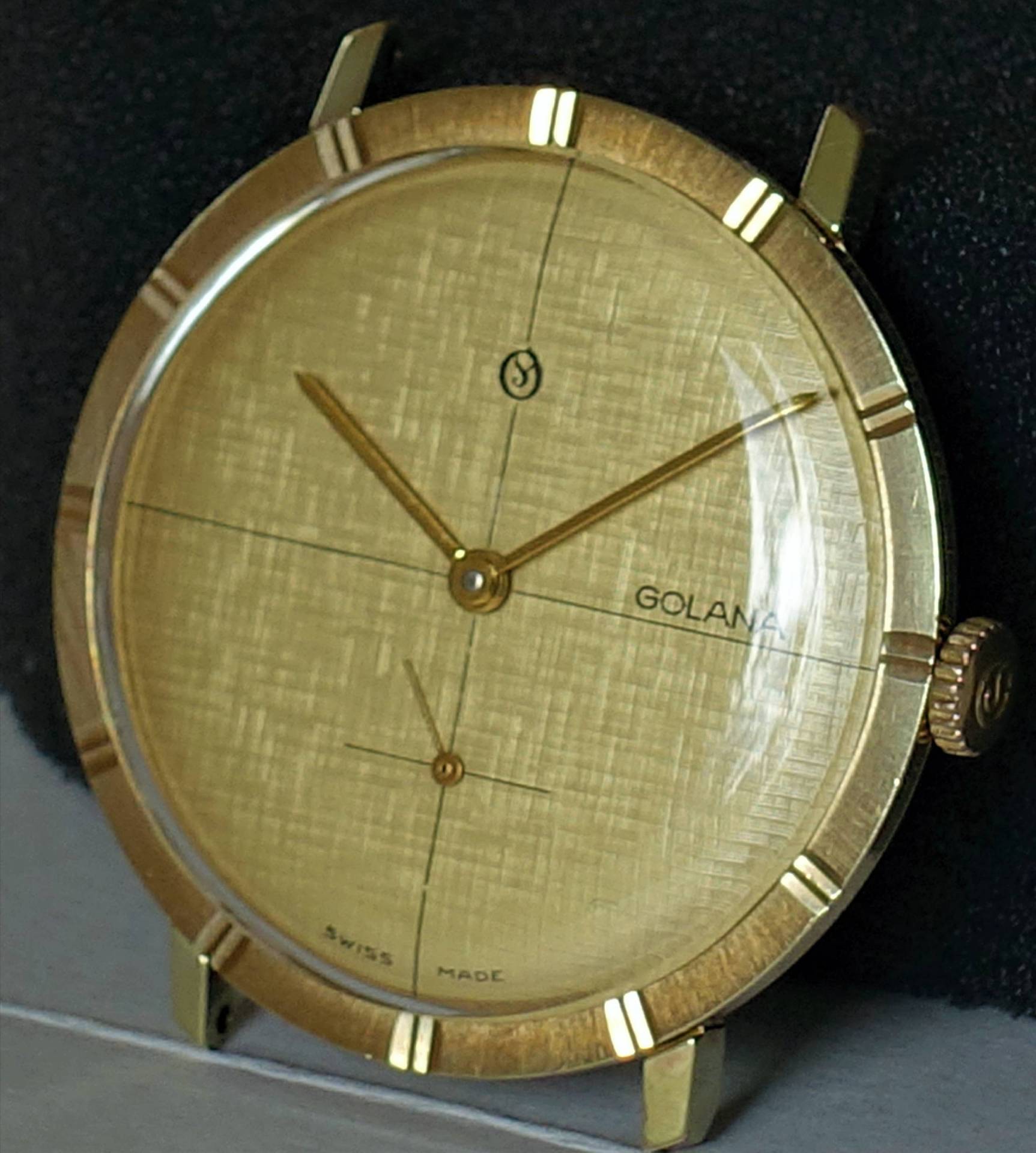 Runde Uhr mit goldfarbenem Gehäuse und Zifferblatt, goldenen Zeigern und feinen Linien auf dem Zifferblatt.