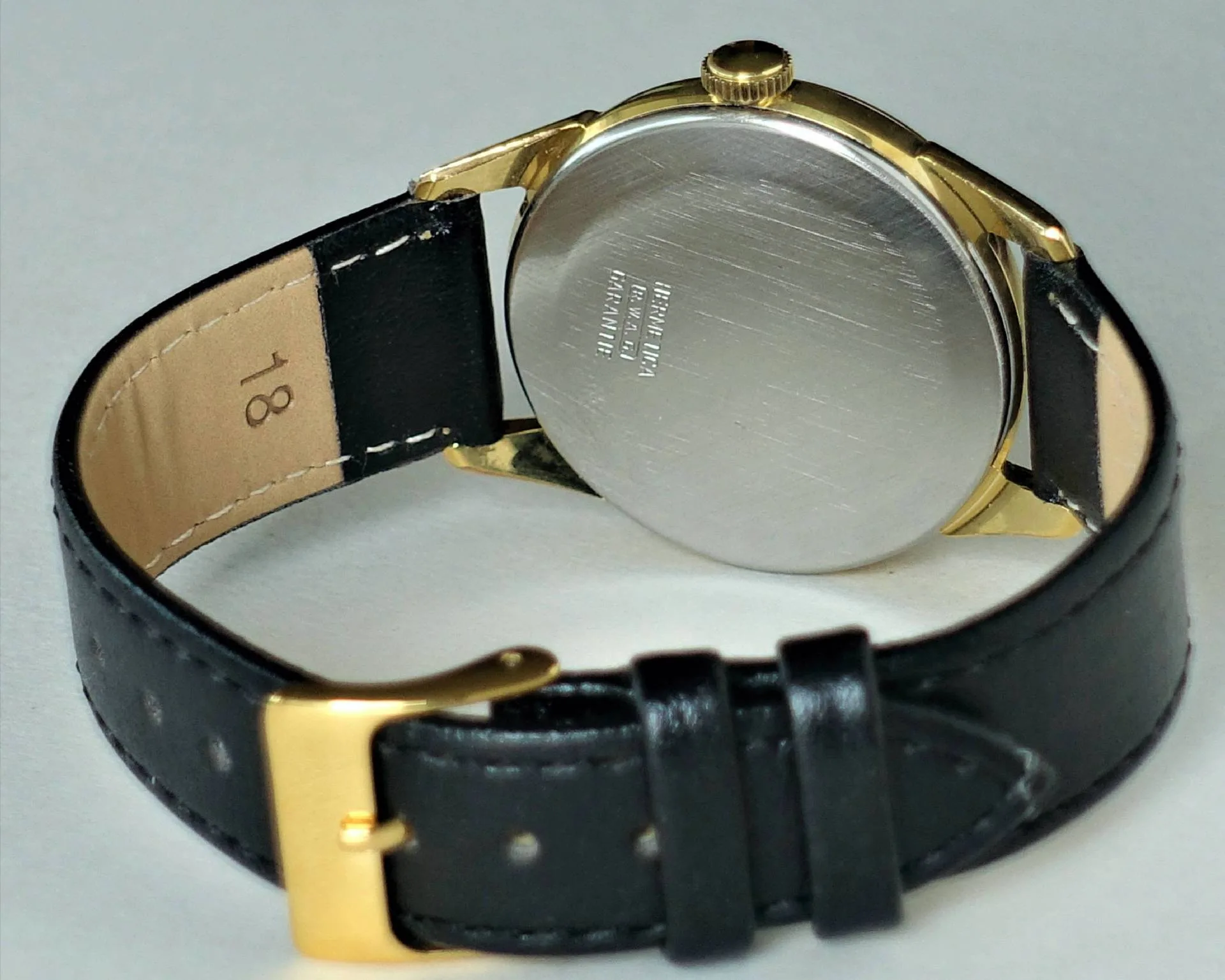 Armbanduhr mit schwarzem Armband, goldfarbenem Gehäuse und silberfarbener Rückseite.
