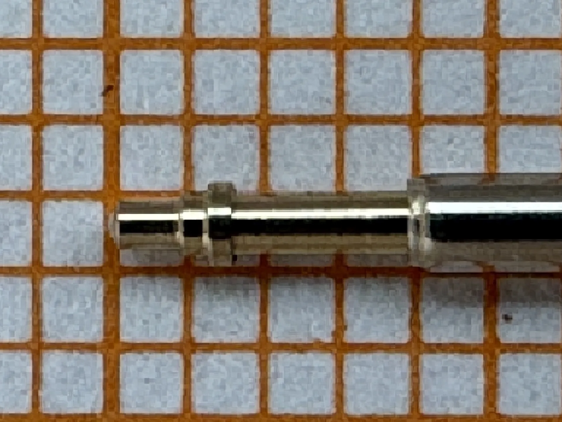 Metallene Aufzugswelle für Armbanduhren, liegend auf kariertem Hintergrund.