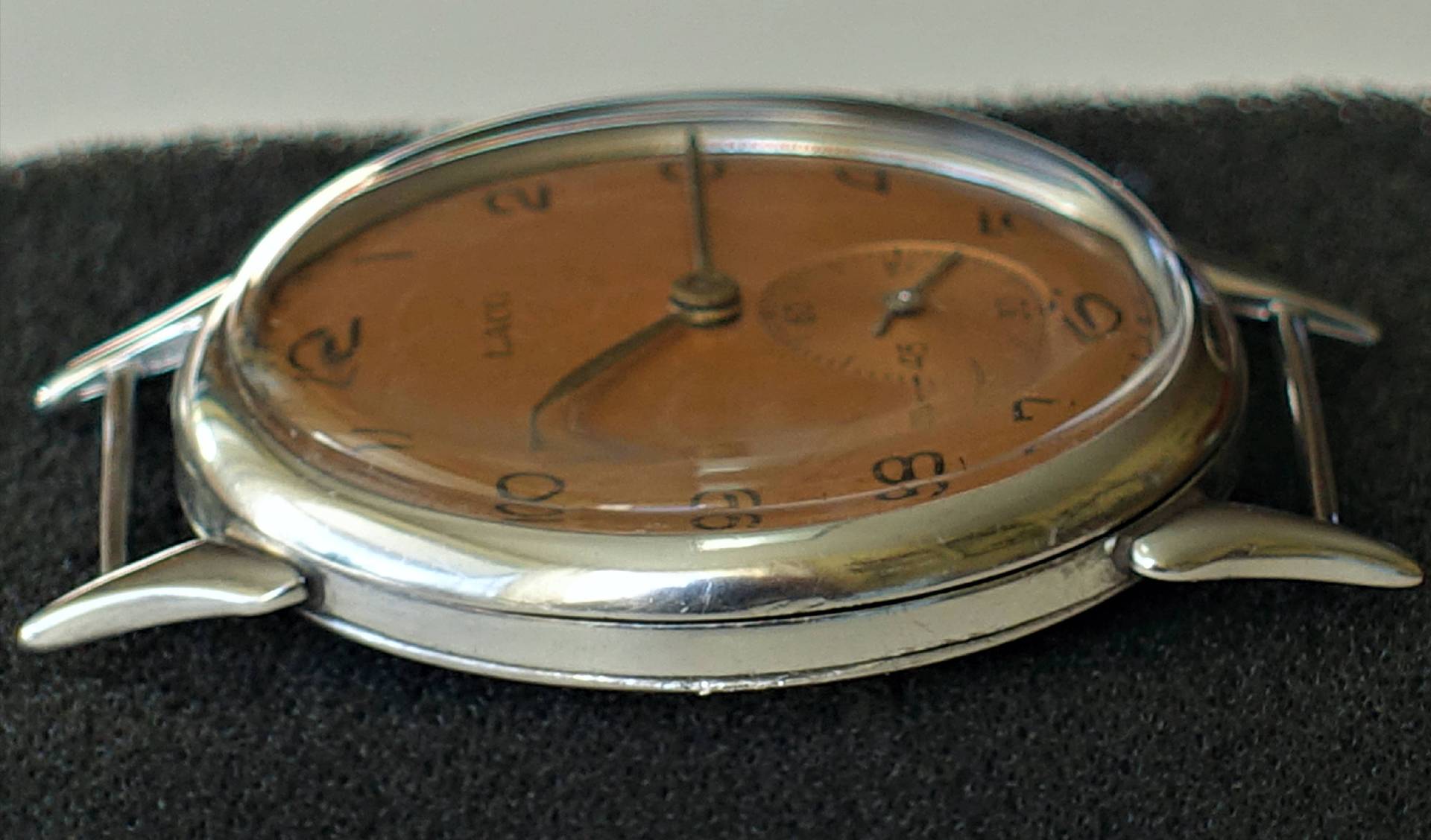 Flache Armbanduhr mit braunem Zifferblatt und silberfarbenem Gehäuse ohne Armband.