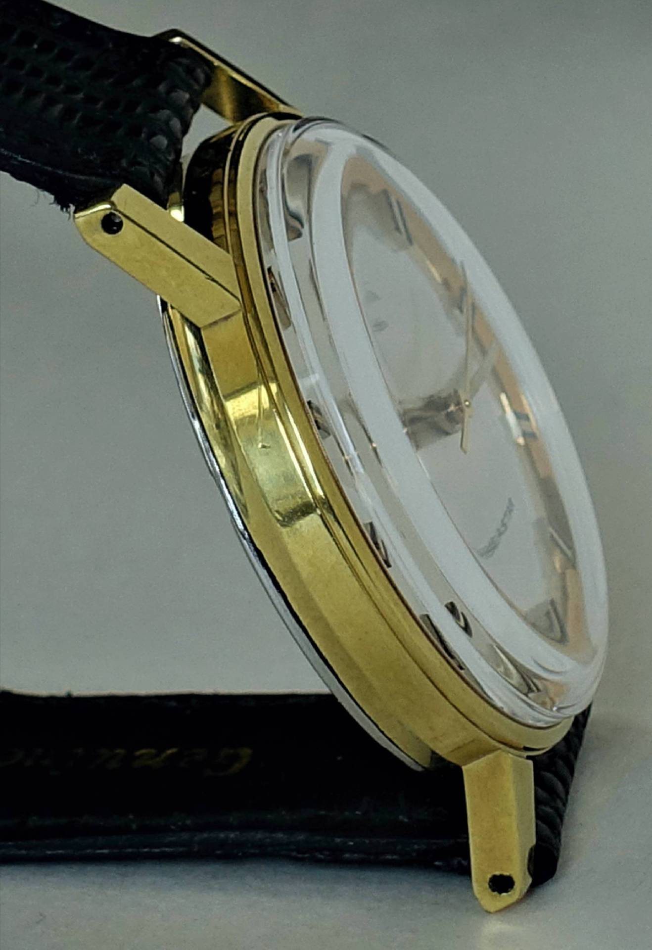 Goldfarbene Armbanduhr mit schwarzem Armband und transparentem Uhrglas.