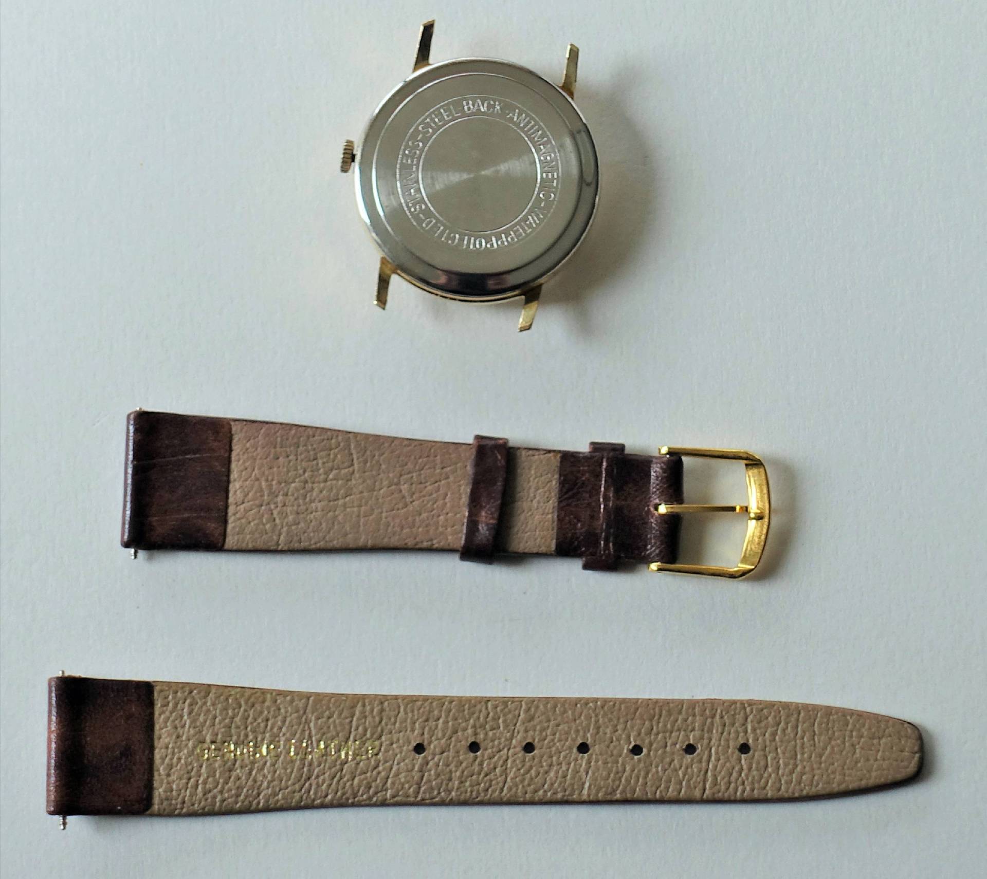 Zerlegtes Uhrgehäuse in silberner Farbe mit braunem Lederarmband und goldfarbener Schließe.