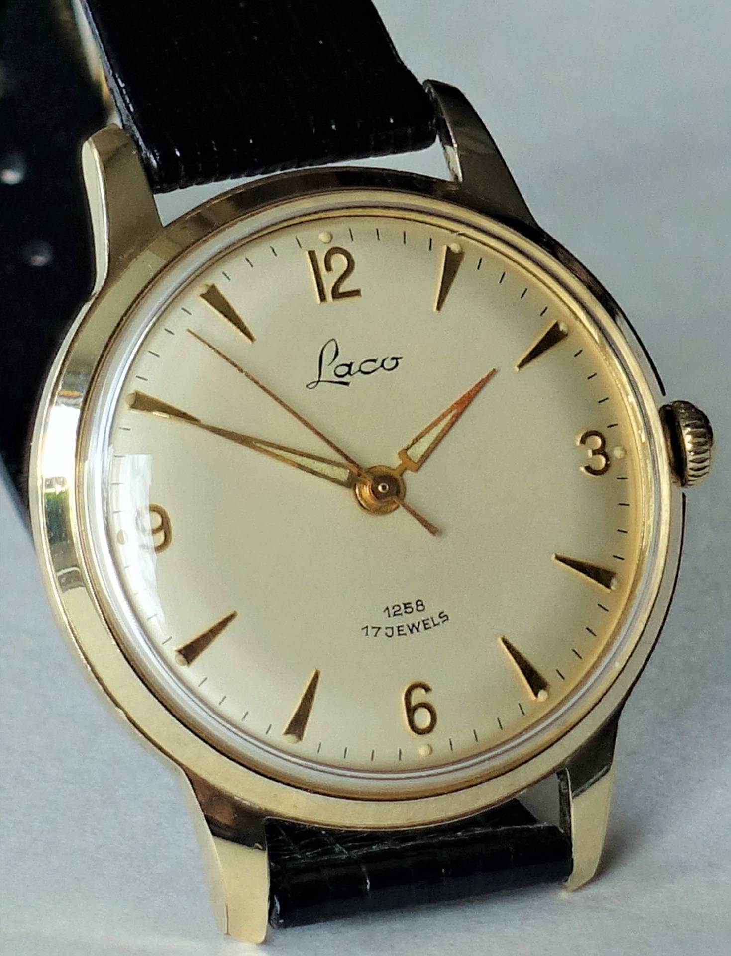 Goldfarbene Armbanduhr mit hellem Zifferblatt und schwarzem Armband.