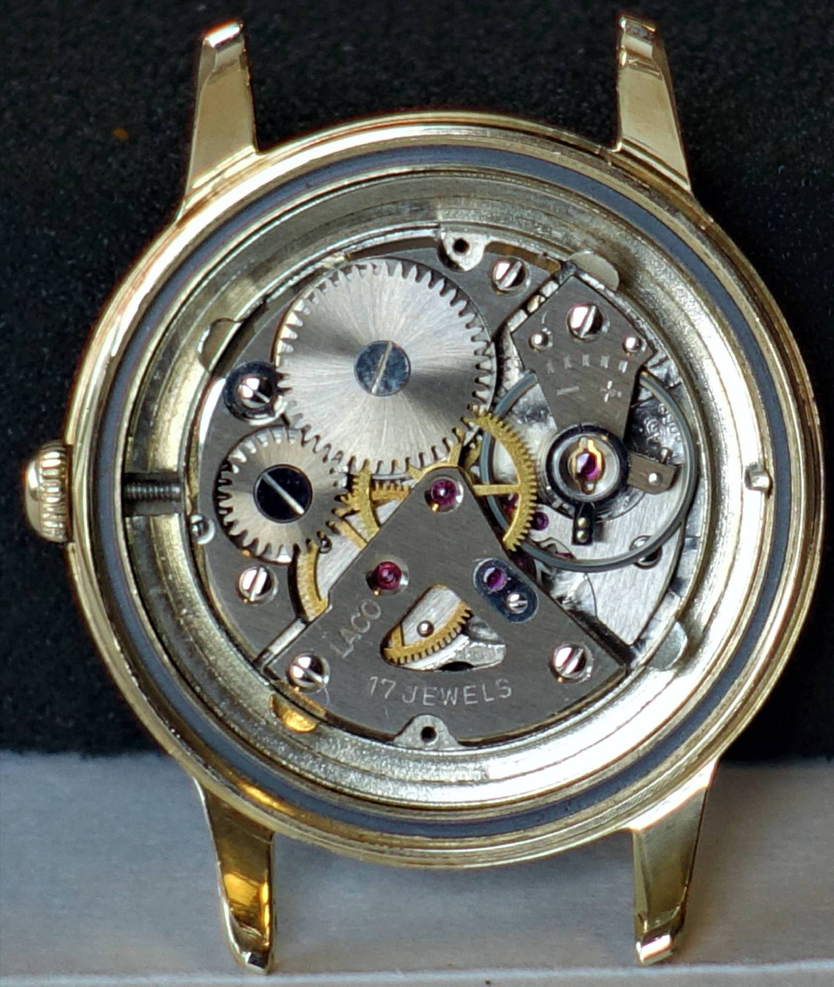 Mechanisches Uhrwerk mit sichtbaren Zahnrädern und der Gravur "Laco 17 Jewels" in einem goldfarbenen Gehäuse.