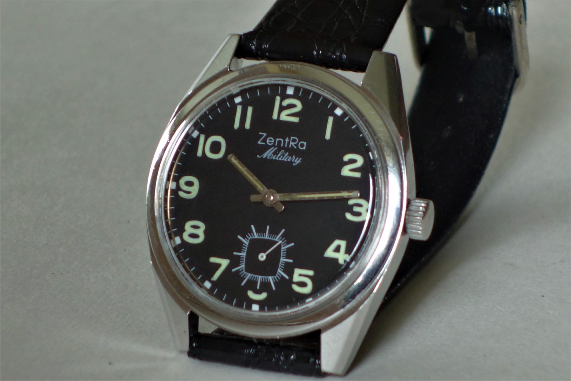 Schwarze Armbanduhr mit silberfarbenem Gehäuse und schwarzem Armband, Zifferblatt mit Leuchtzahlen und kleiner Sekunde.