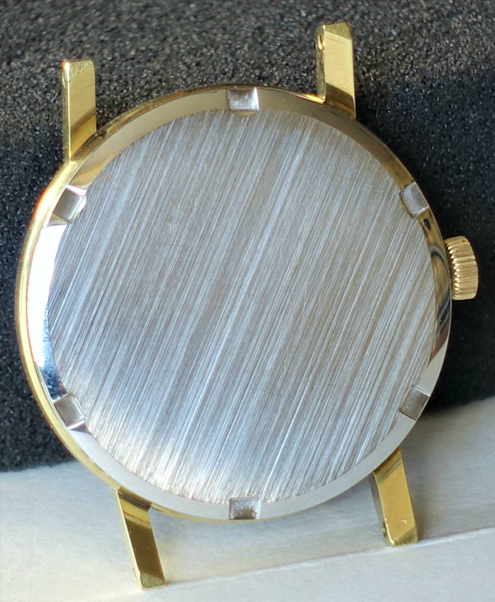 Rundes Uhrengehäuse mit silberfarbener Rückseite und goldfarbenen Hörnern.