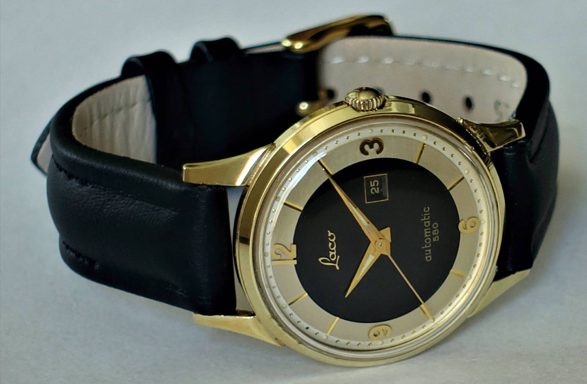 Schwarze Armbanduhr mit goldfarbenem Gehäuse und schwarzem Lederarmband.