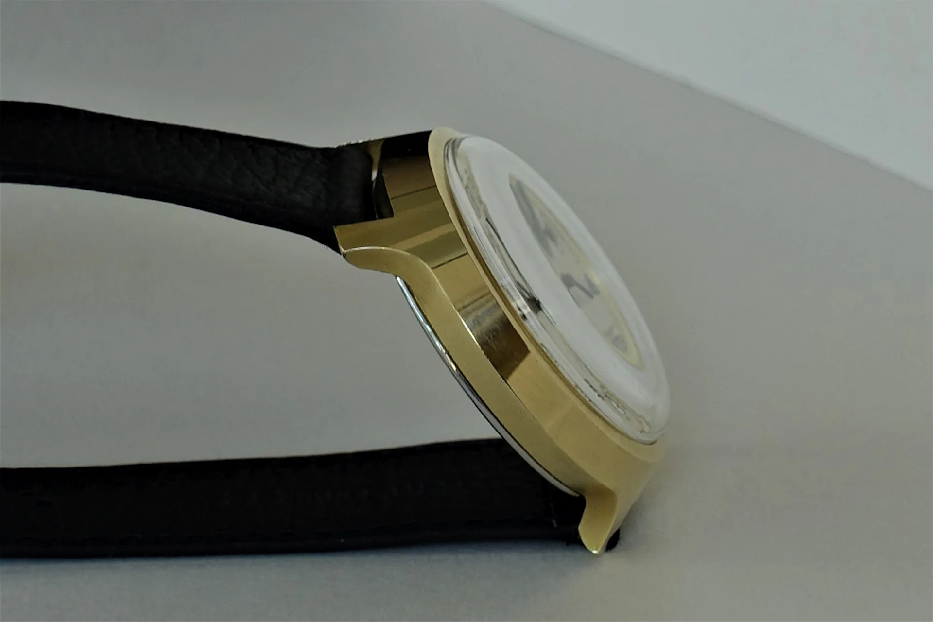 Uhr mit schwarzem Armband Armbanduhr mit goldfarbenem Gehäuse und schwarzem Armband in Seitenansicht.