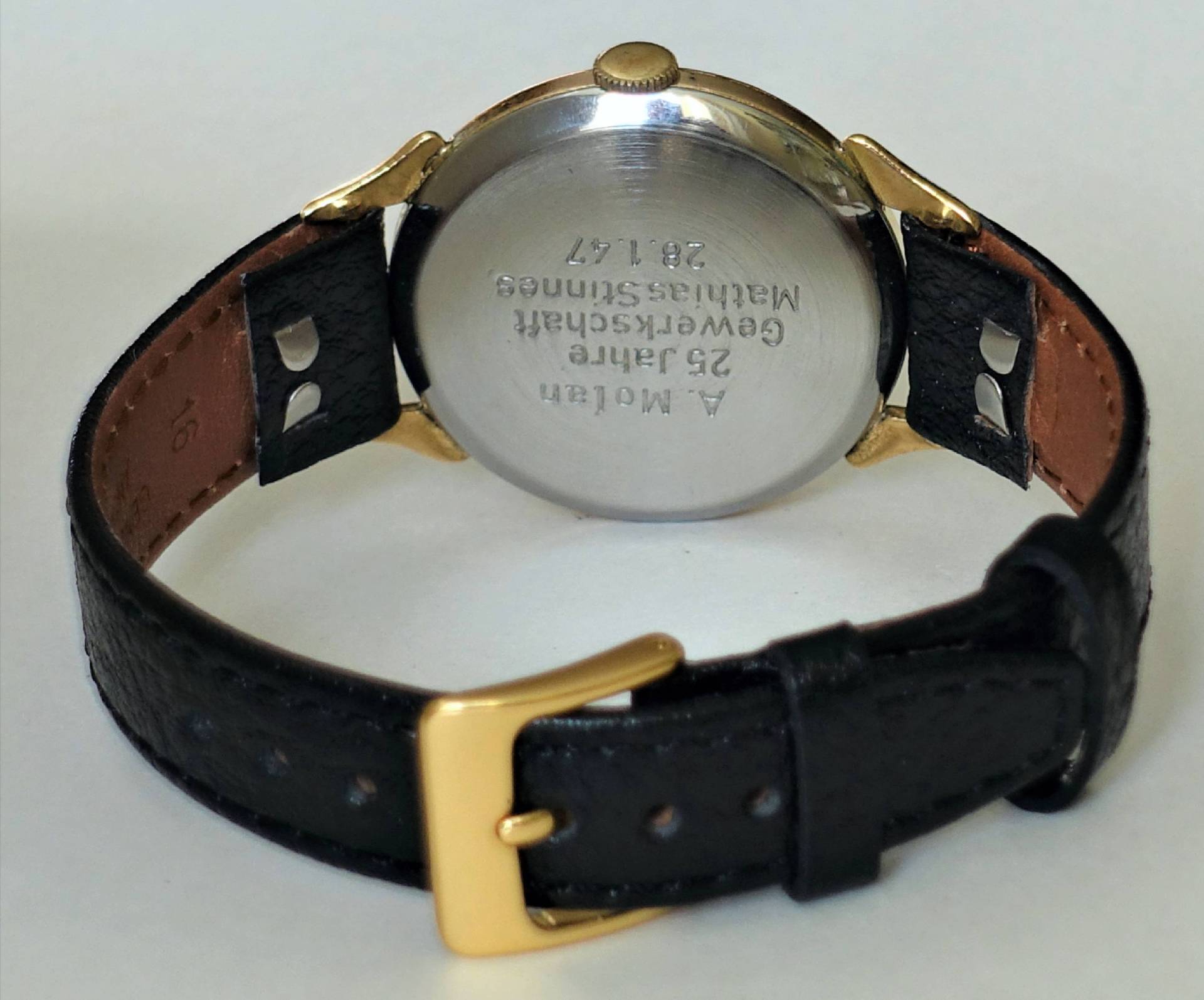 Schwarze Armbanduhr mit goldfarbenen Elementen und silberfarbener Rückseite.