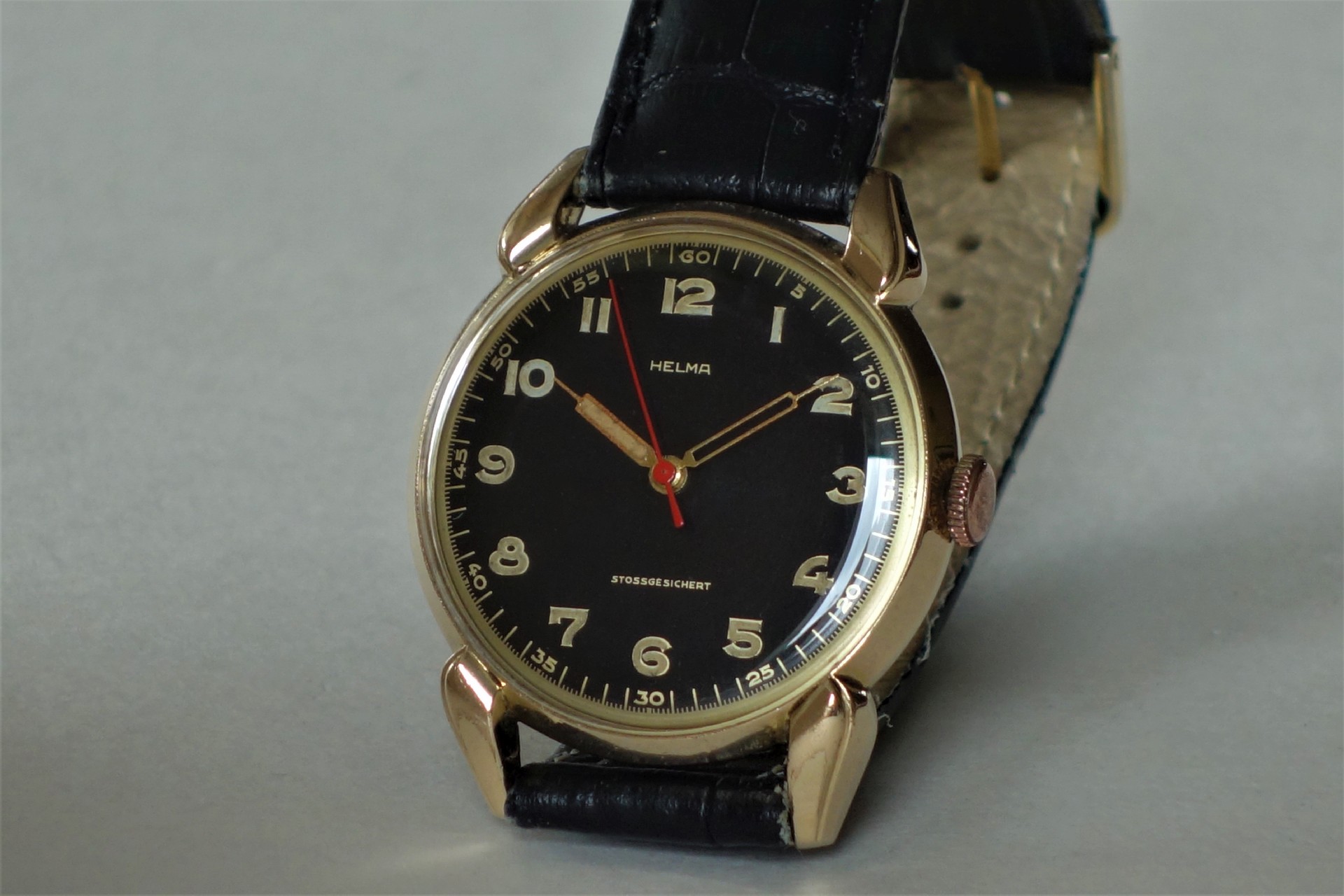 Schwarze Armbanduhr mit goldfarbenem Gehäuse und schwarzem Armband.