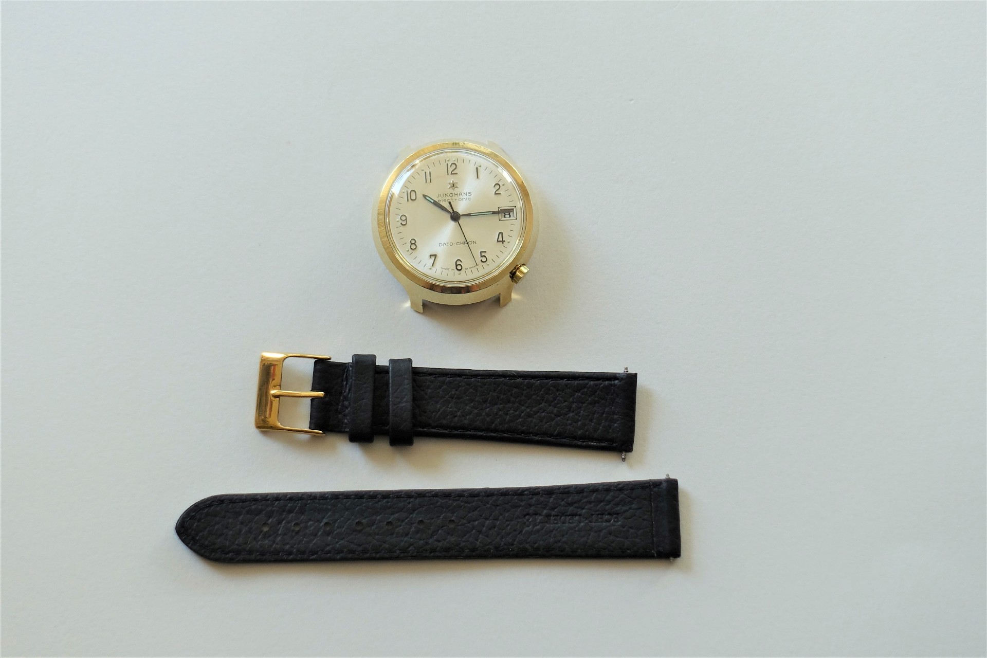 Zerlegtes Uhrgehäuse in goldfarbener Optik mit schwarzem Lederarmband und goldfarbener Schließe.