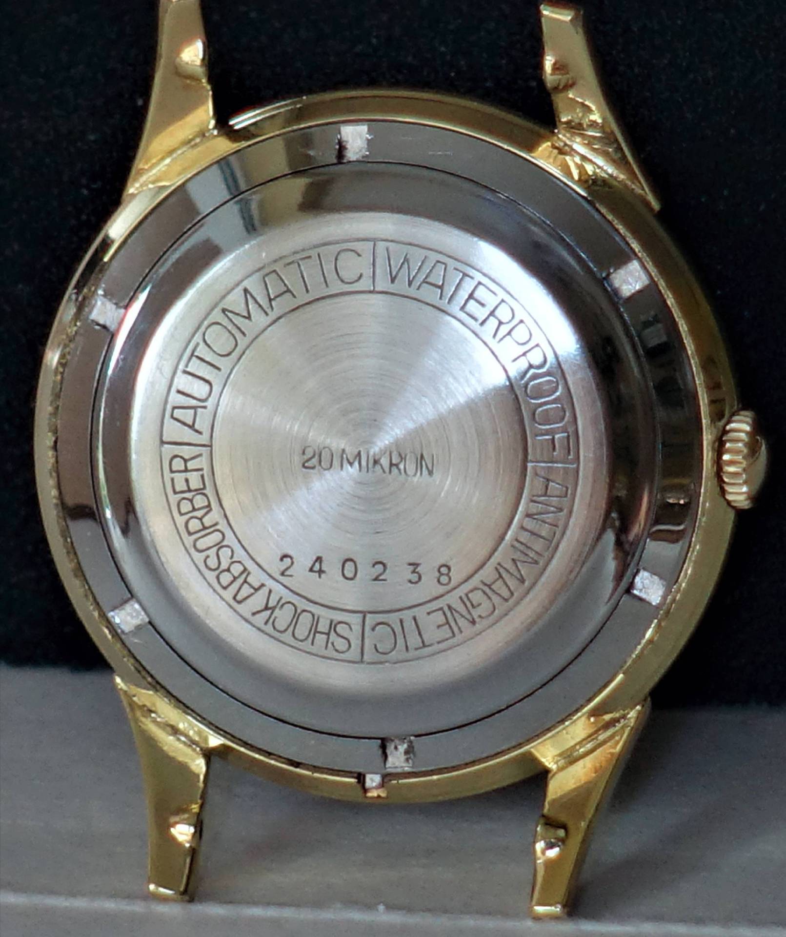 Rückseite eines goldfarbenen und silbernen Uhrengehäuses mit Gravur und Seriennummer.