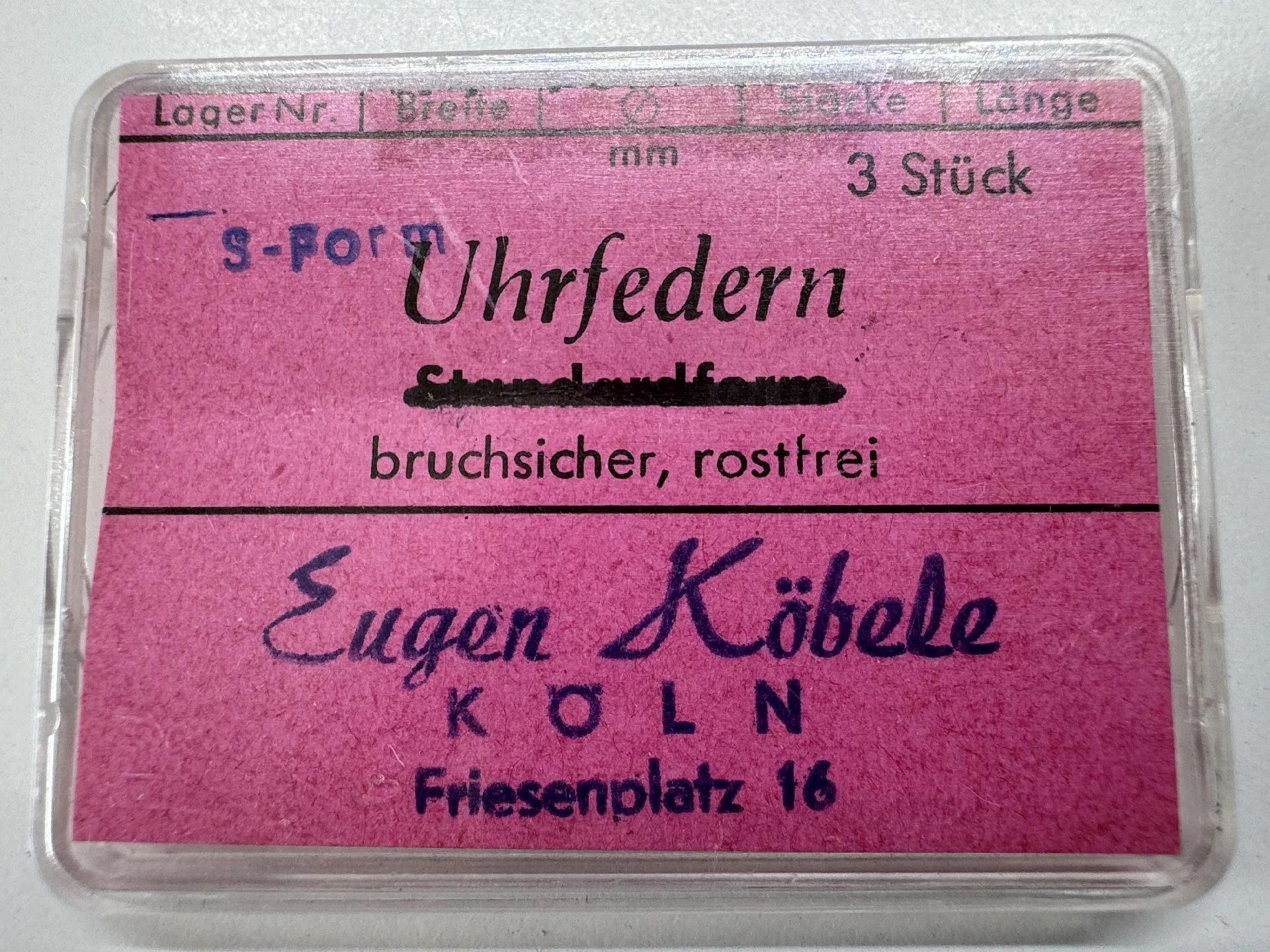 Drei bruchsichere und rostfreie Uhrfedern in S-Form in einer transparenten Kunststoffbox mit pinkem Etikett.