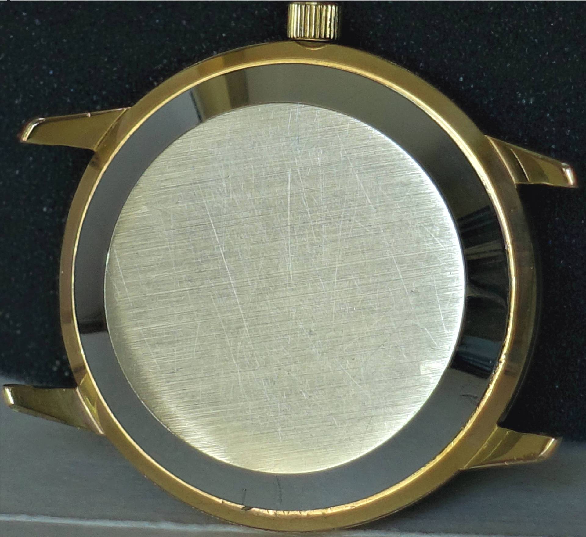 Rundes Uhrengehäuse in goldfarbener Optik mit silberfarbener Rückseite.