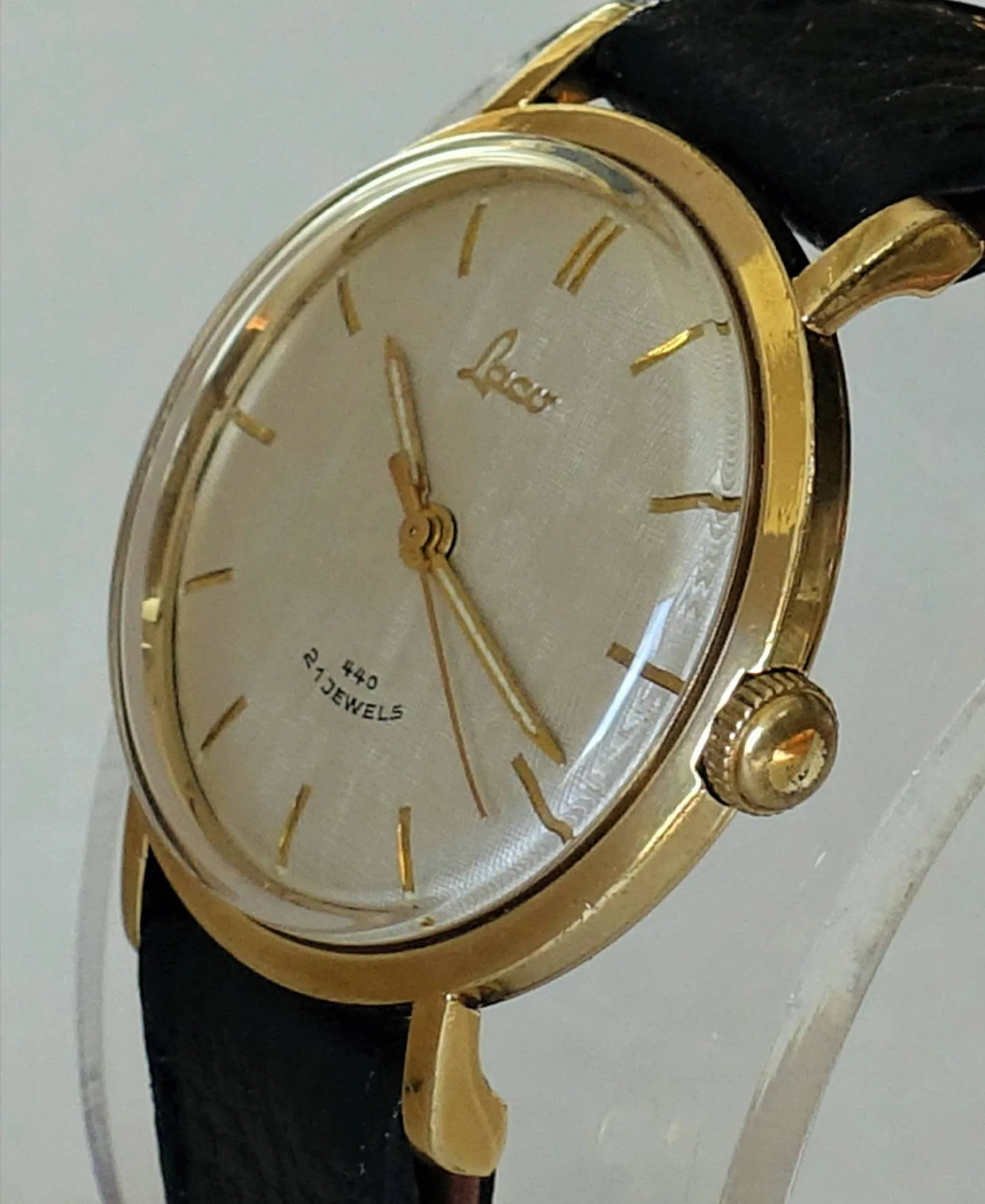 Analoge Armbanduhr mit goldfarbenem Gehäuse, hellem Zifferblatt und schwarzem Armband.