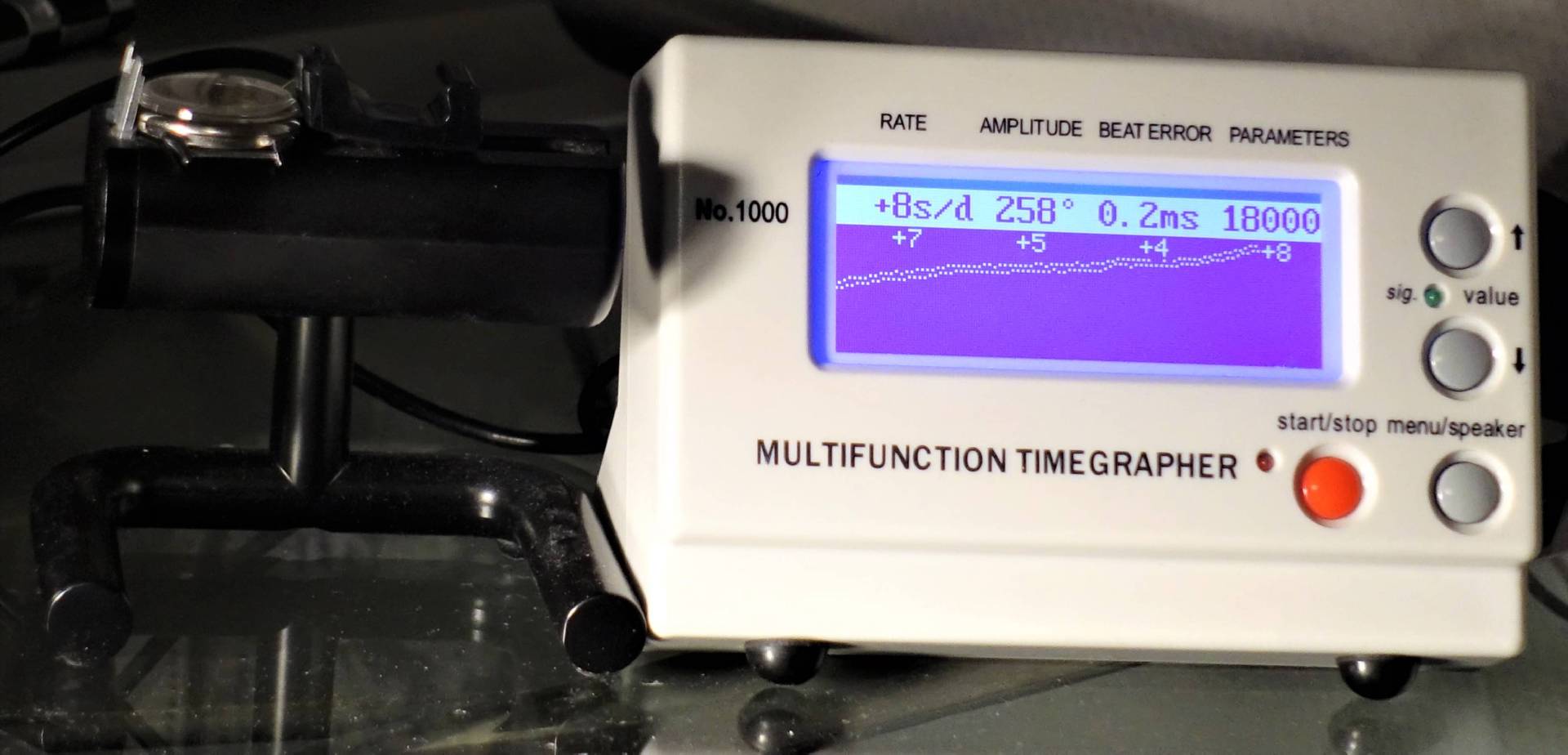 Weißes elektronisches Messgerät zur Analyse mechanischer Uhren mit digitalem Display und Bedientasten.