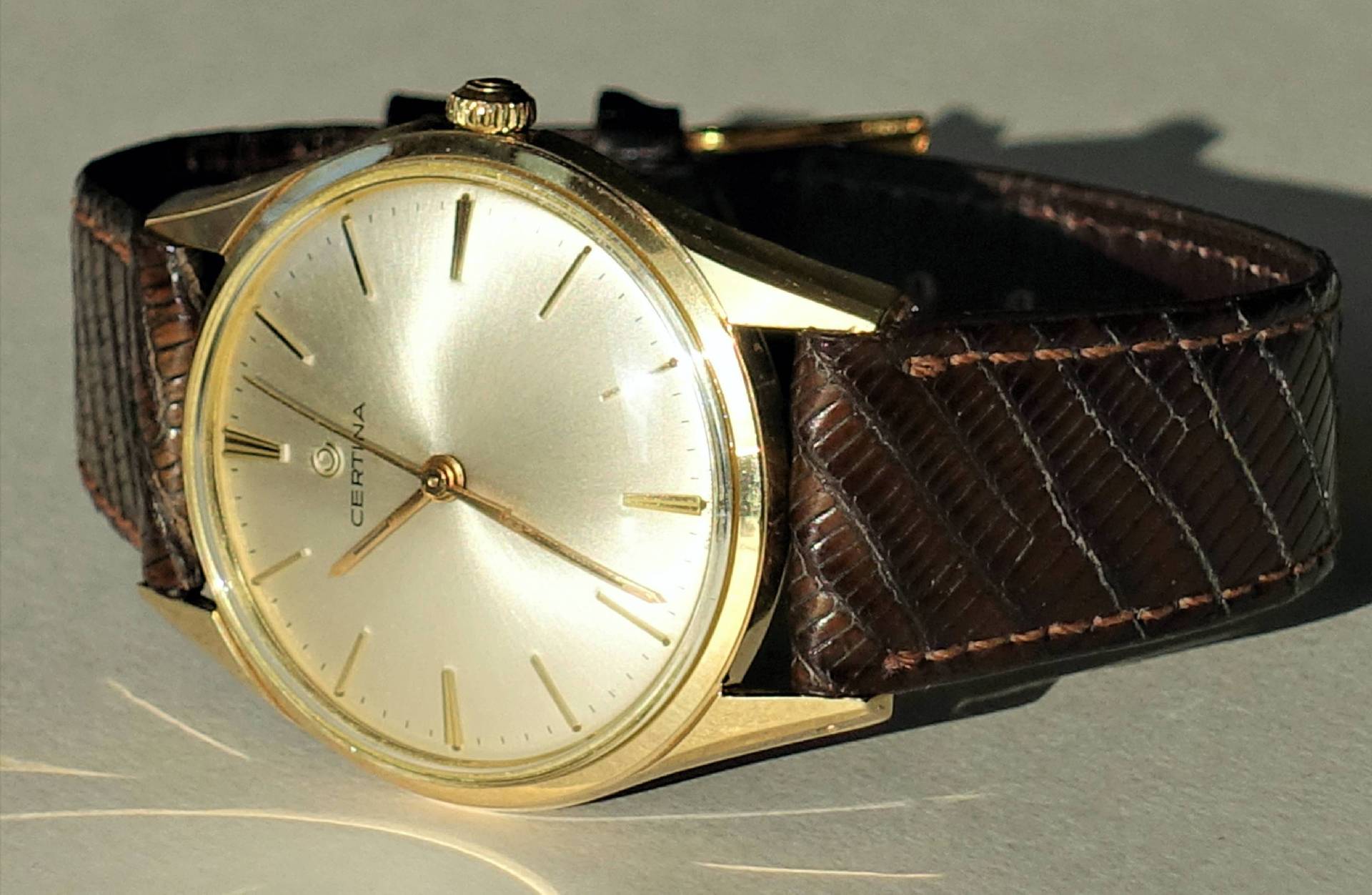 Goldfarbene Armbanduhr mit hellem Zifferblatt und braunem Armband.