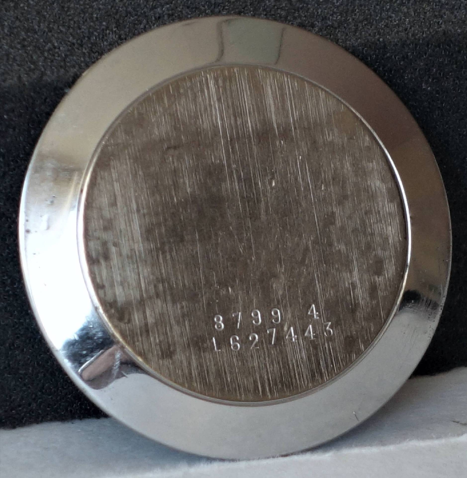 Runder silberfarbener Uhrenboden mit eingravierten Zahlen.